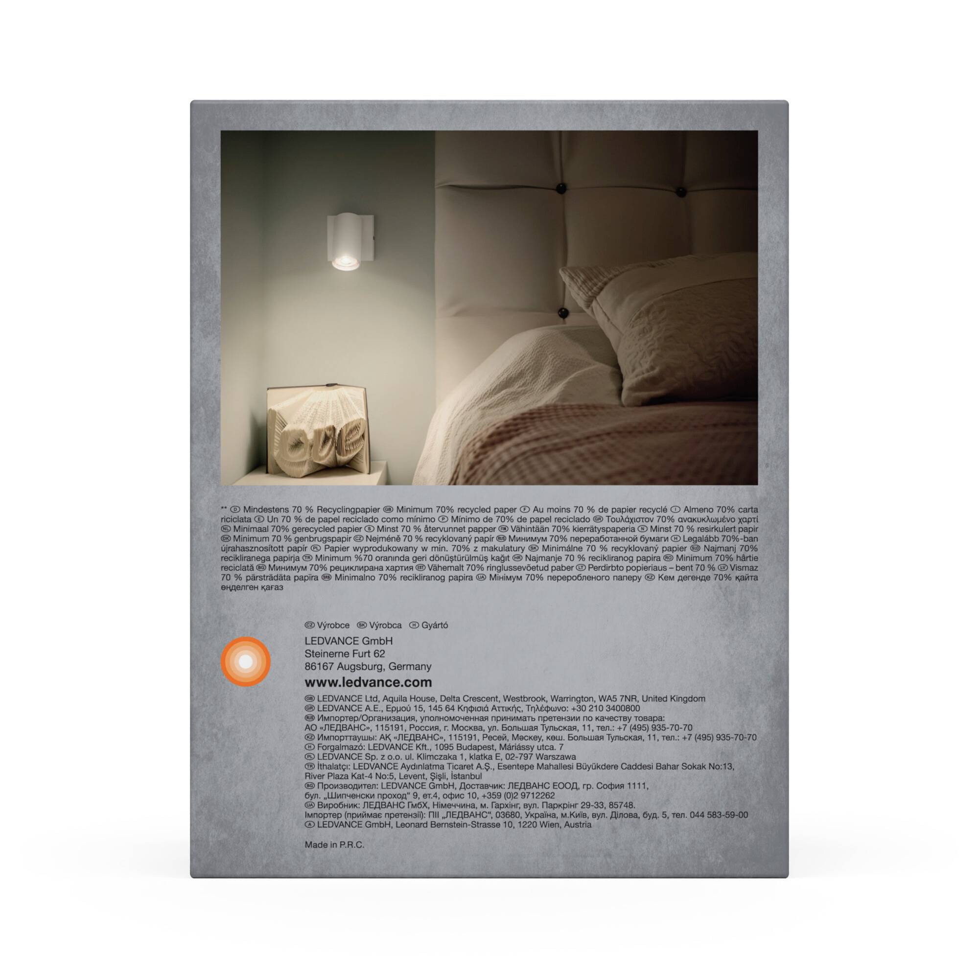 Et sengebord med digital ur og lampe ved siden af en seng med polstret hovedgærde i et moderne indrettet rum.