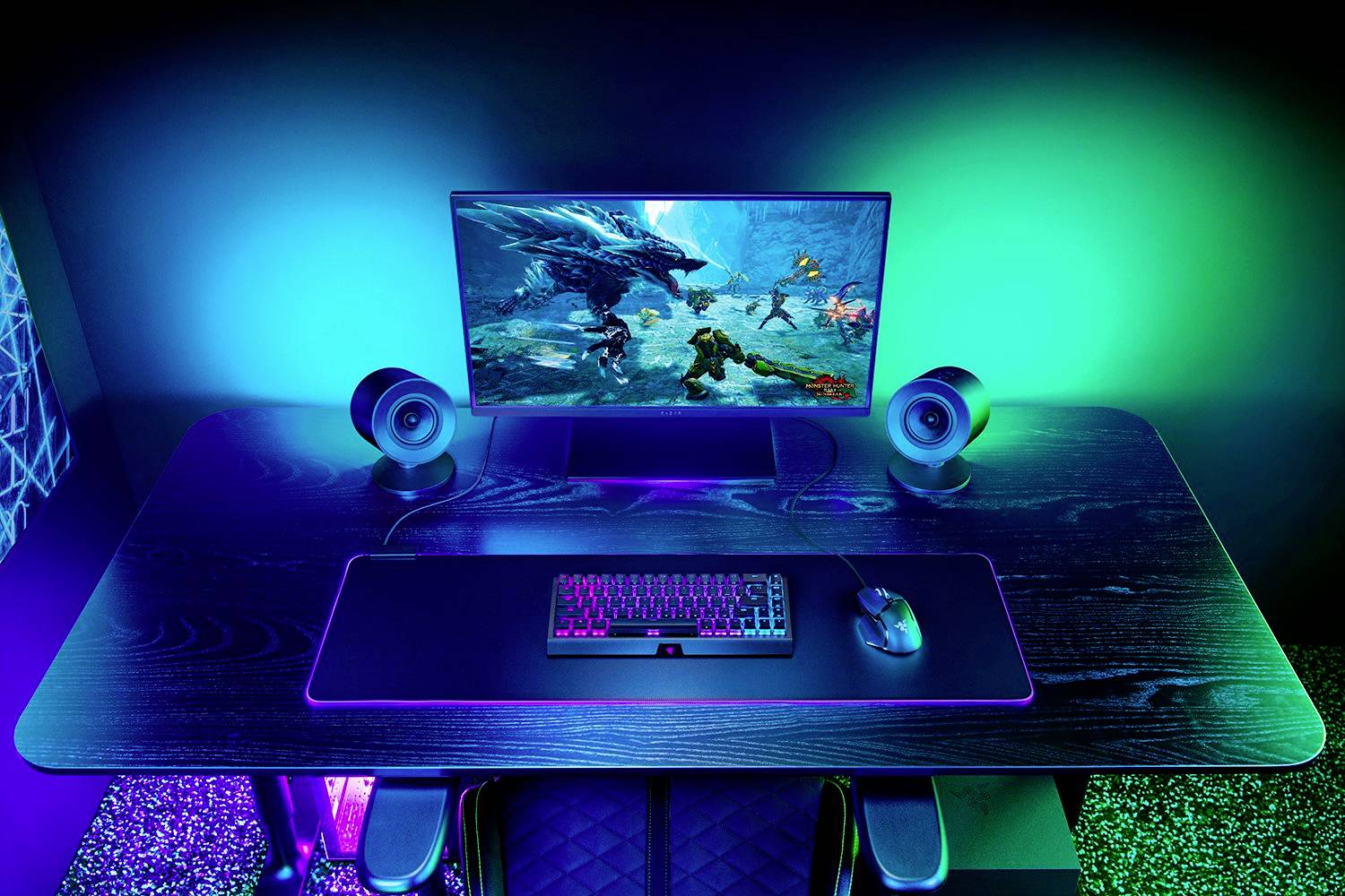 Et ergonomisk gaming-skrivebord med belyst skærm, tastatur og mus, alle badet i blåt, grønt og violet lys.