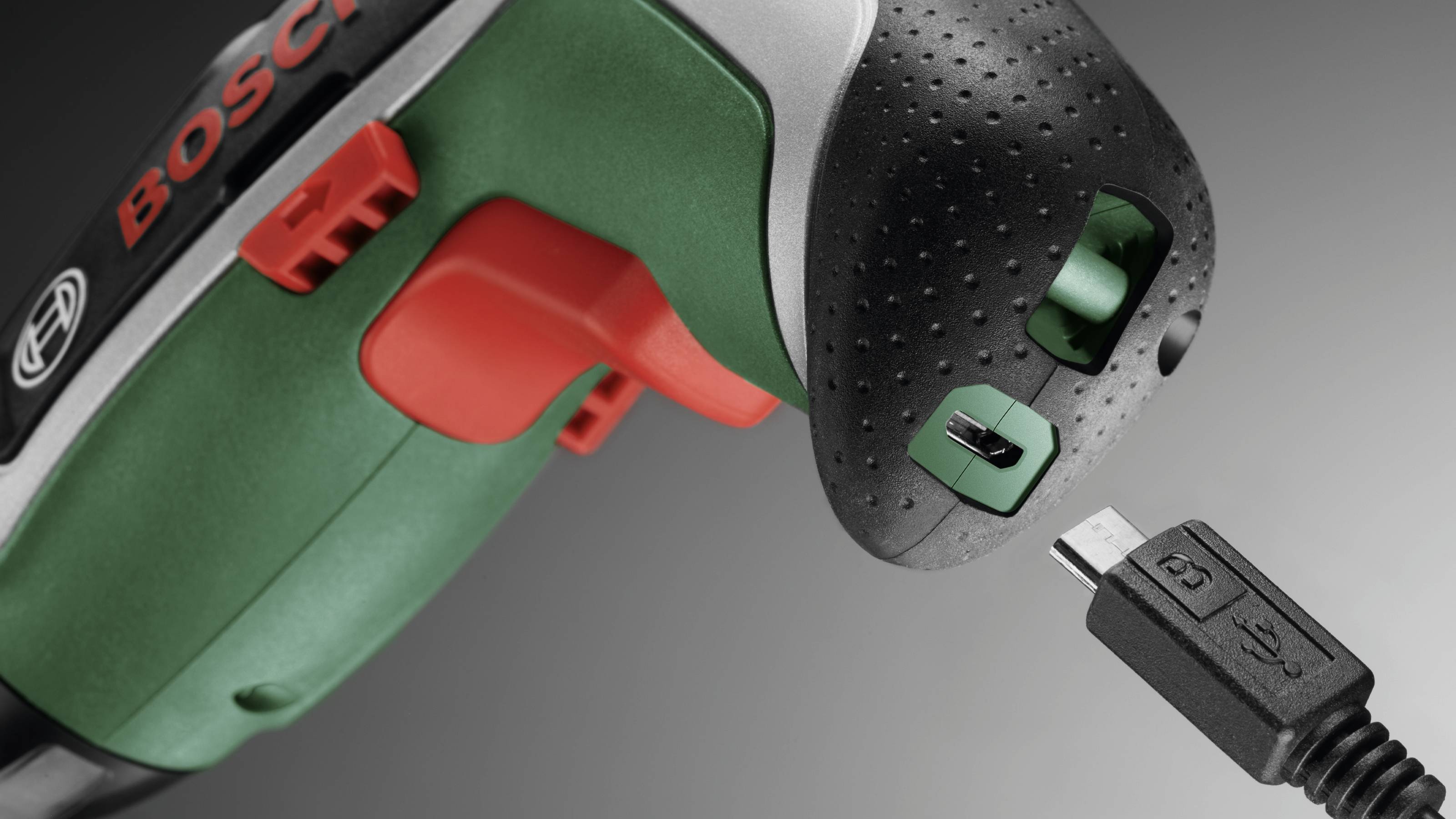 Akku-skruemaskine i nærbillede med fokus på opladningsporten, ved siden af ligger et passende USB-kabel til opladning.