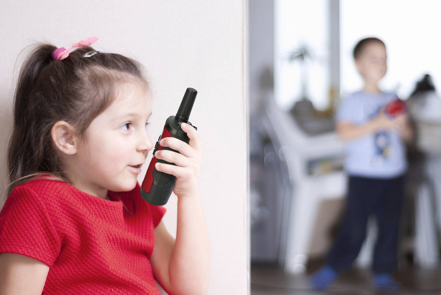 Et pigebarn taler i en walkie-talkie, mens en dreng i baggrunden også holder en. De leger tydeligt sammen.