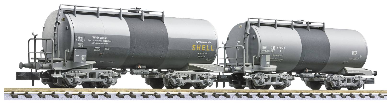 To tanke med Shell-mærkning, begge i grå farve, er placeret på jernbaneskinner. Køretøjerne er fremstillet til transport af væsker og fremstår i bevægelse.