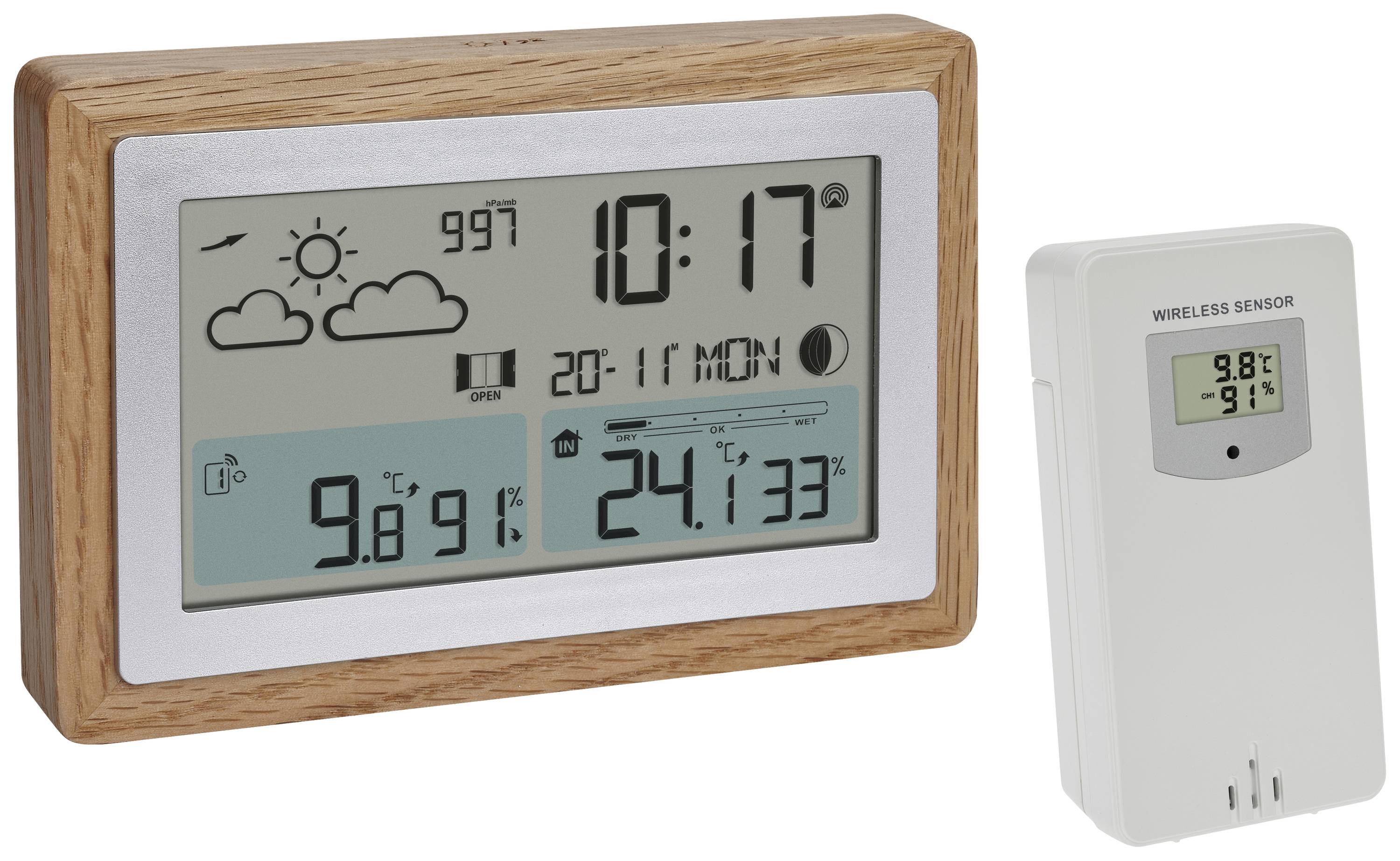 Digitalt termometer med træramme viser vejrdata: Sol, lufttryk, temperatur indendørs '24,1°C', udendørs '9,8°C'. Trådløs sensor ved siden af.