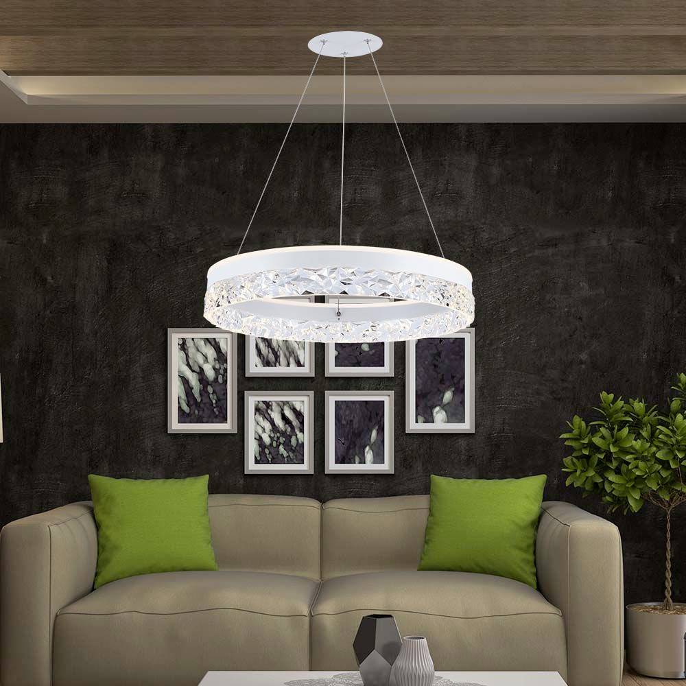 Stue med grå sofa, grønne puder, moderne malerier på væggen, en lysekrone og en plante i hjørnet.