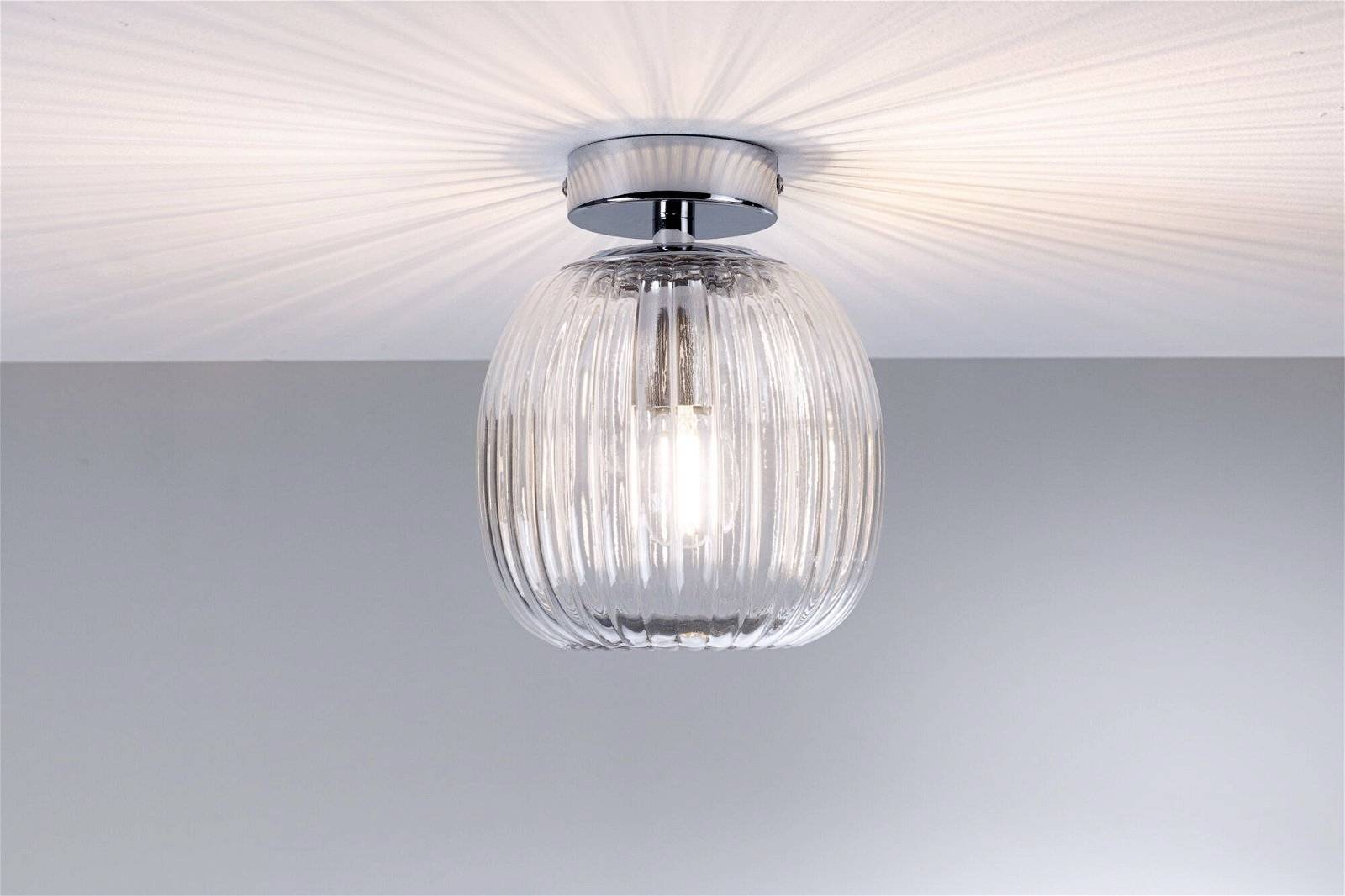 En loftslampe med riflet, klart glasskærm, der sender et blidt, diffust lys op på den hvide loft.