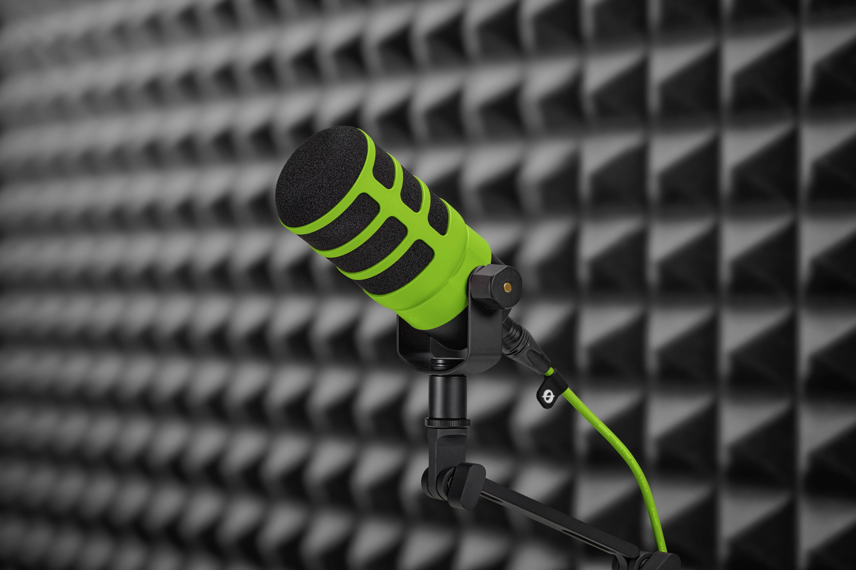Grøn mikrofon på et stativ i et rum med lydabsorberende skumvægge, velegnet til optagelser eller podcasts.