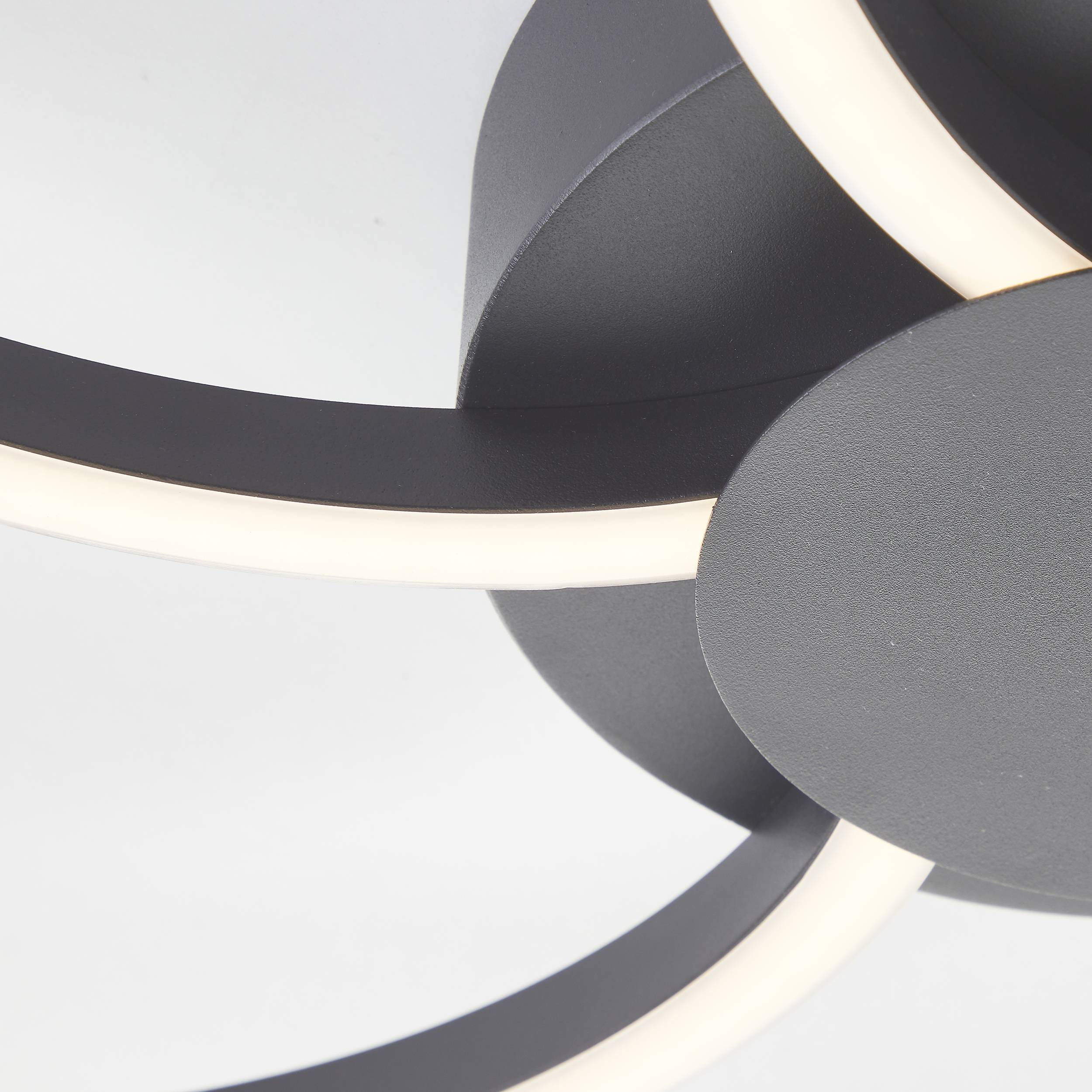 En moderne, abstrakt LED-loftslampe med overlappende, buede metalstrimler og indbyggede, lysende striber.