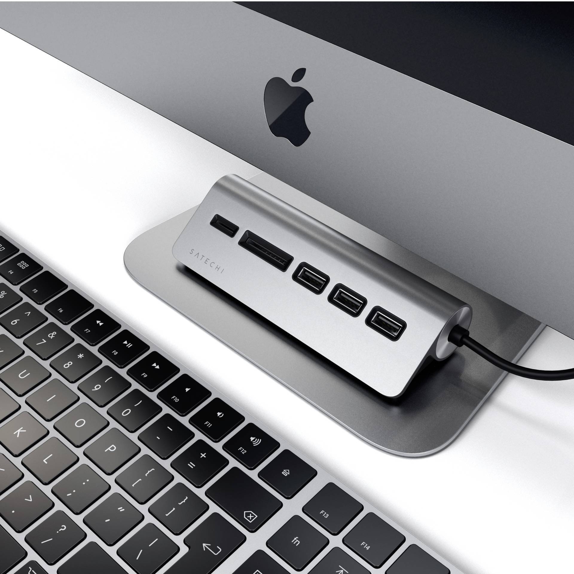 En sølvfarvet USB-C-hub med fire porte er tilsluttet en computer ved siden af et sort tastatur og en bærbar computer.