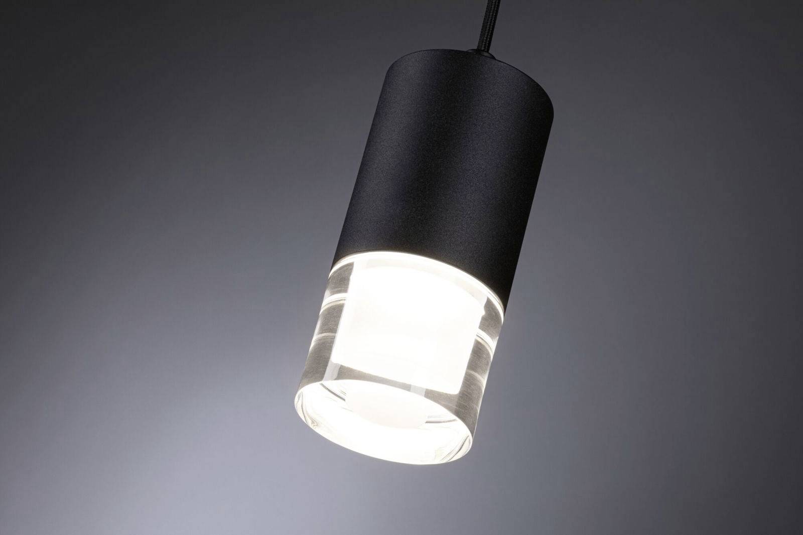 En hængende sort lampe med en gennemsigtig nedre del lyser op i et mørkt rum.