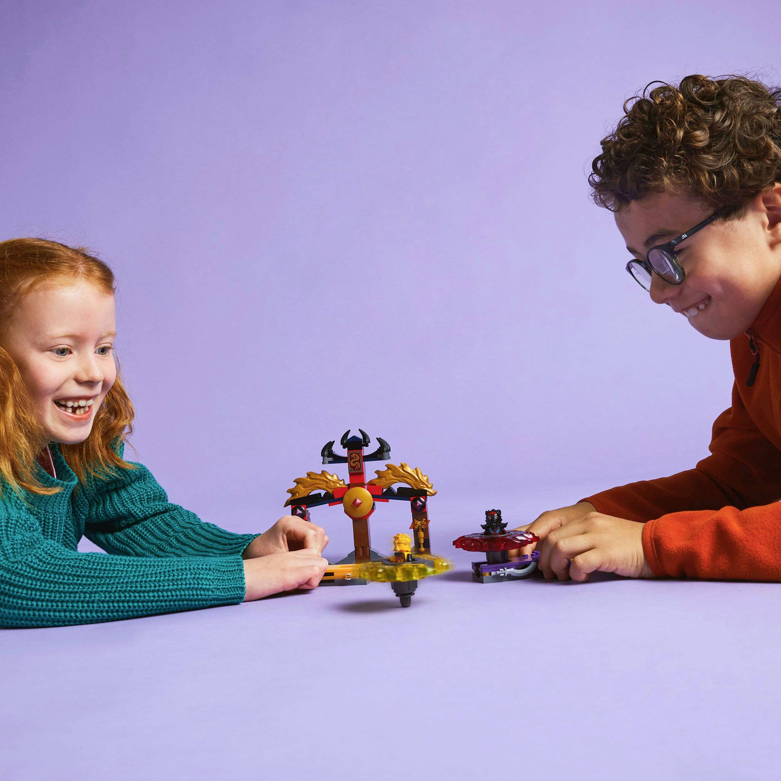 Et pige og en dreng leger med et lille, farverigt legesæt, der er formet som en top.