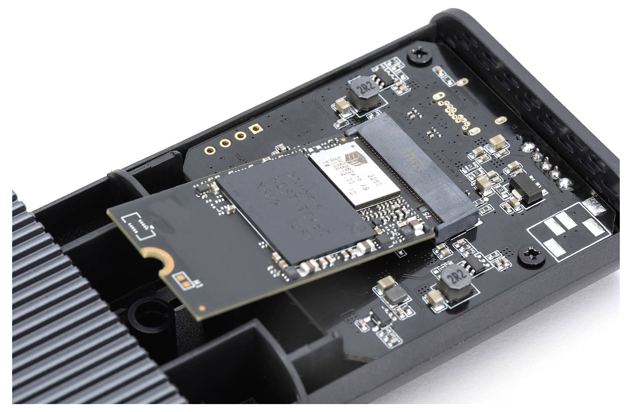 Nærbillede af et åbnet SSD-kabinet med en synlig M.2-SSD monteret på et bundkort, omgivet af elektroniske komponenter.