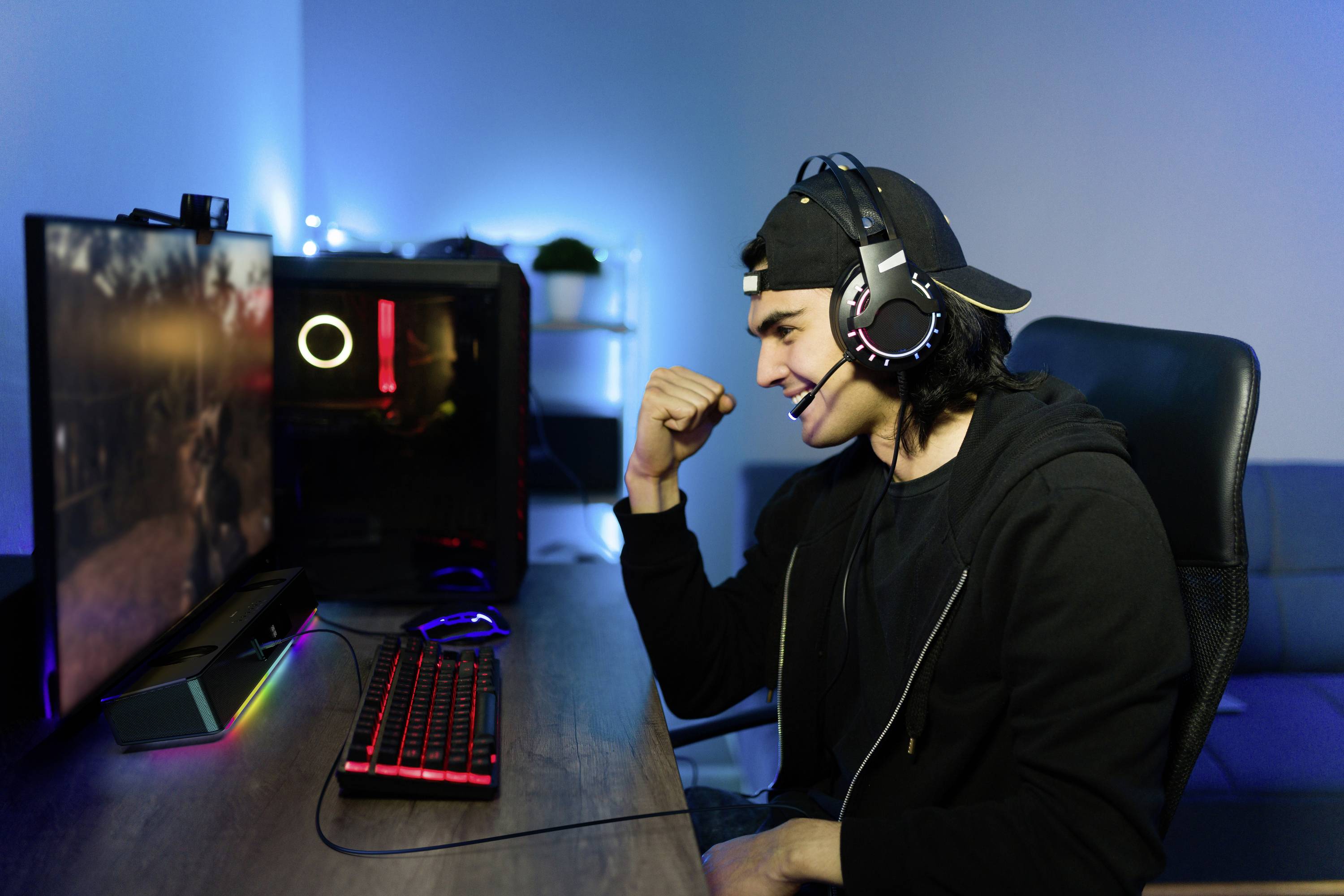 En ung mand sidder foran en computerskærm, har et headset på og smiler, mens han spiller et videospil.