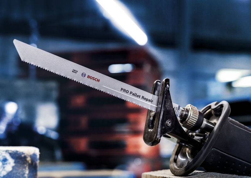 En sav med påskriften 'PRO Pallet Repair' vises fra siden i et værksted. I baggrunden ses slørede paller.