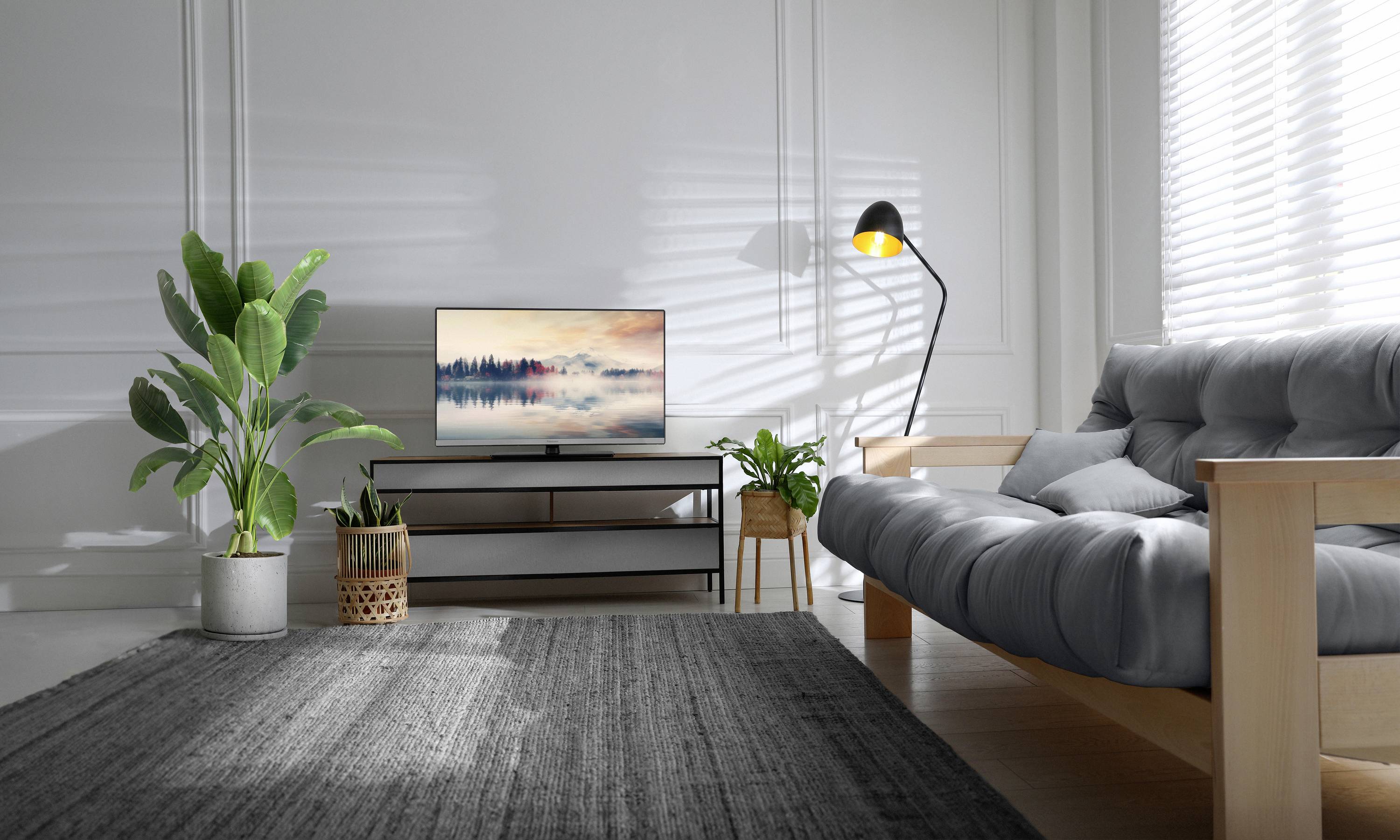 Et stue med en moderne sofa, tæppe, planter og et fladskærms-tv på en reol. Belysningen er hyggelig.