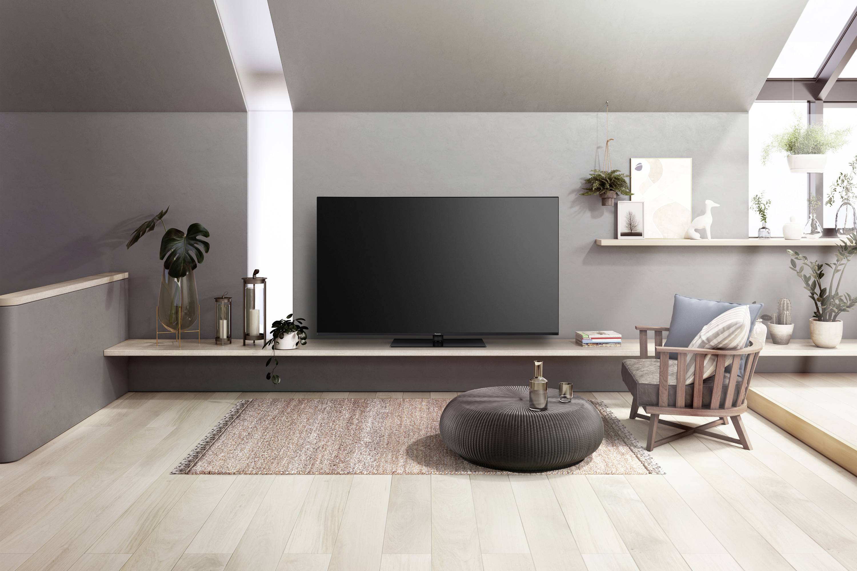 Et moderne, minimalistisk opholdsrum med et fladskærms-tv på en reol, planter, en lænestol og en puf på et tæppe.
