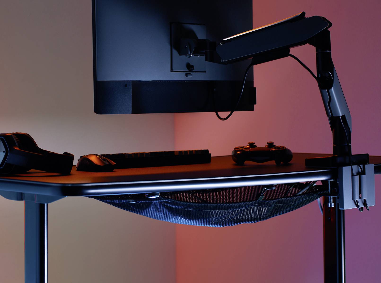 'Skrivebord med skærm, tastatur, headset og controller. Belysningen er blå og lyserød, hvilket skaber en afslappet atmosfære.'
