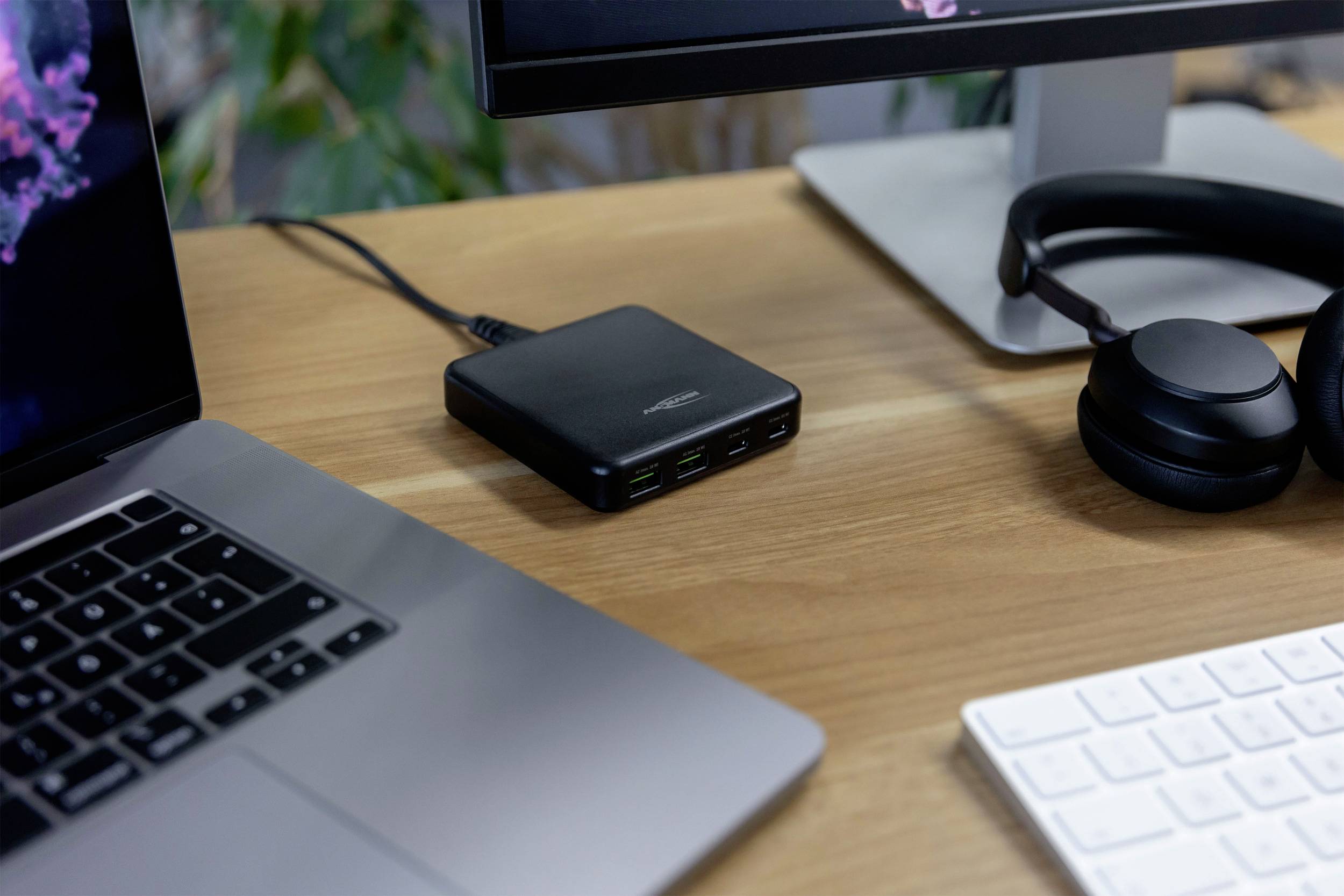 På et skrivebord står en bærbar computer, en skærm, et par høretelefoner og en multi-USB-opladestation. Teknisk arbejdsplads.