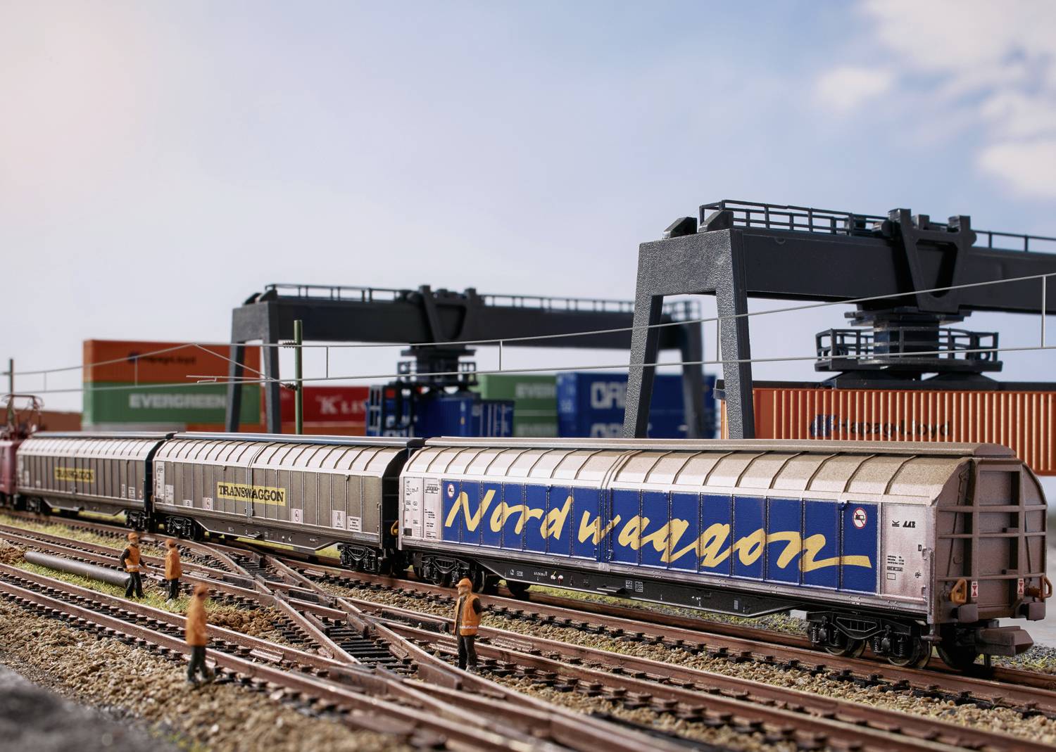 Modeltogsscene med godstog på skinnerne og kraner i baggrunden. Arbejdere står langs med sporene.