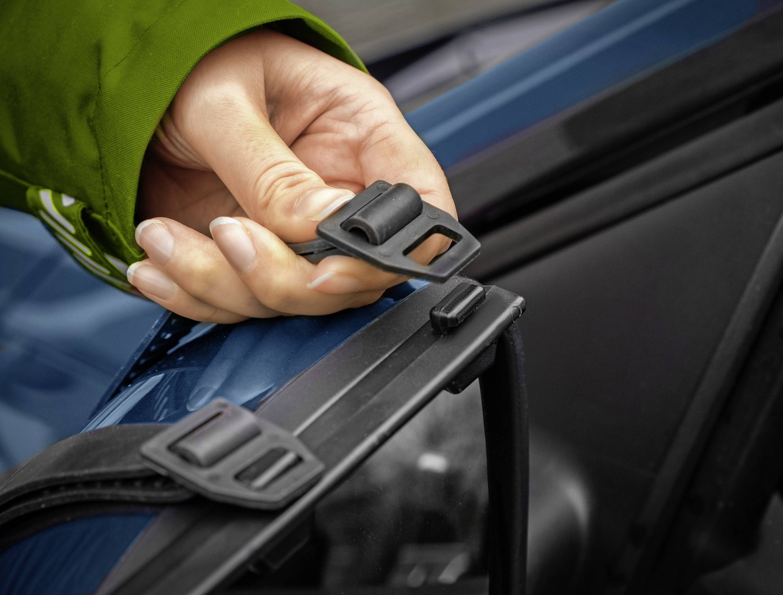 En person peger på en vinduesvisker, iført en grøn jakke. Fokus er på et fastgørelsesclips.