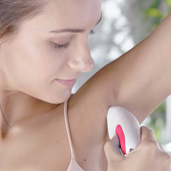 En person bruger en hvid elektrisk epilator til at fjerne armhulehår. Omgivelserne er godt oplyste.