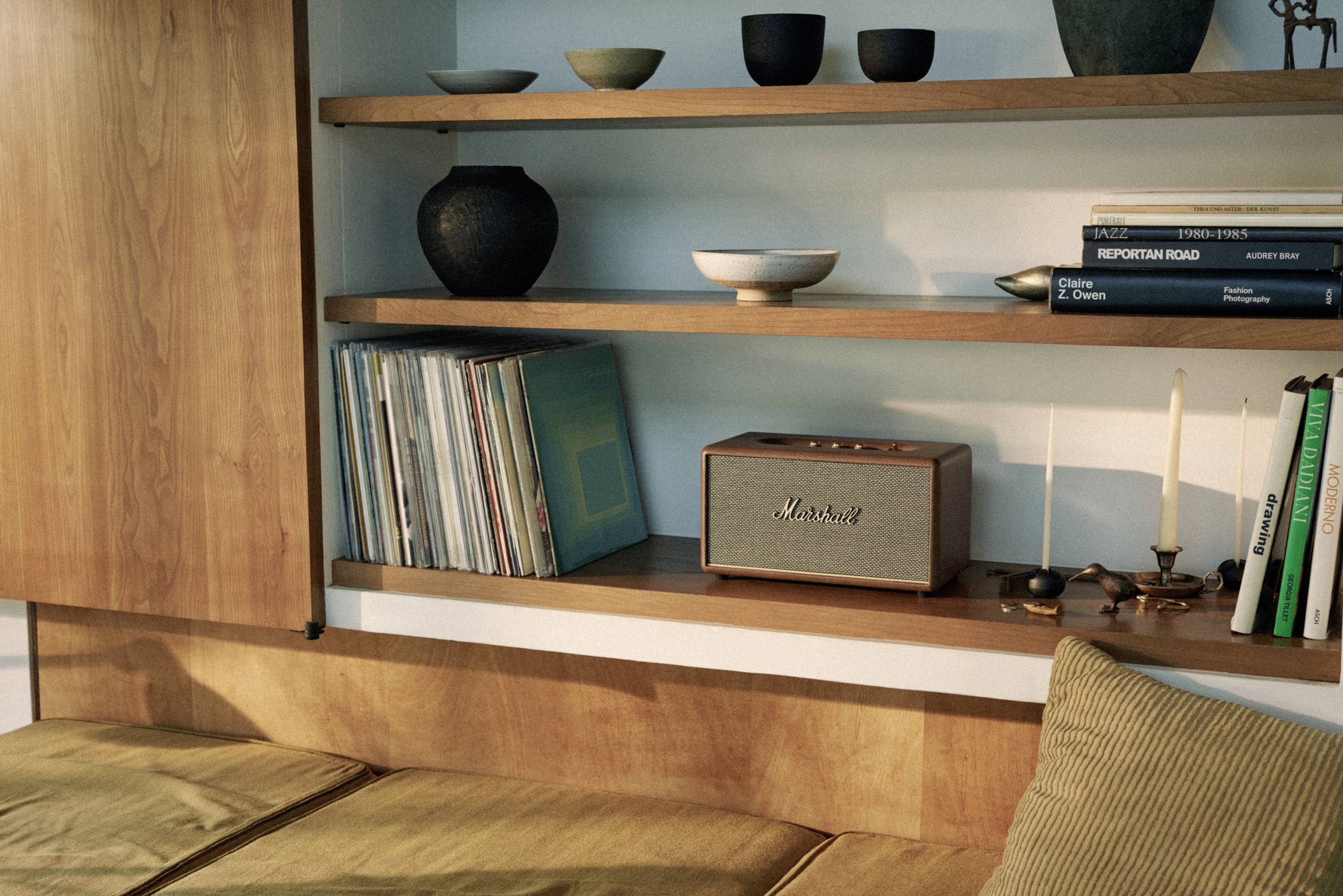 Reol med vinylplader, keramiske skåle, bøger og en højtaler. Under reolen en sofa med puder. Retro og hyggelig atmosfære.