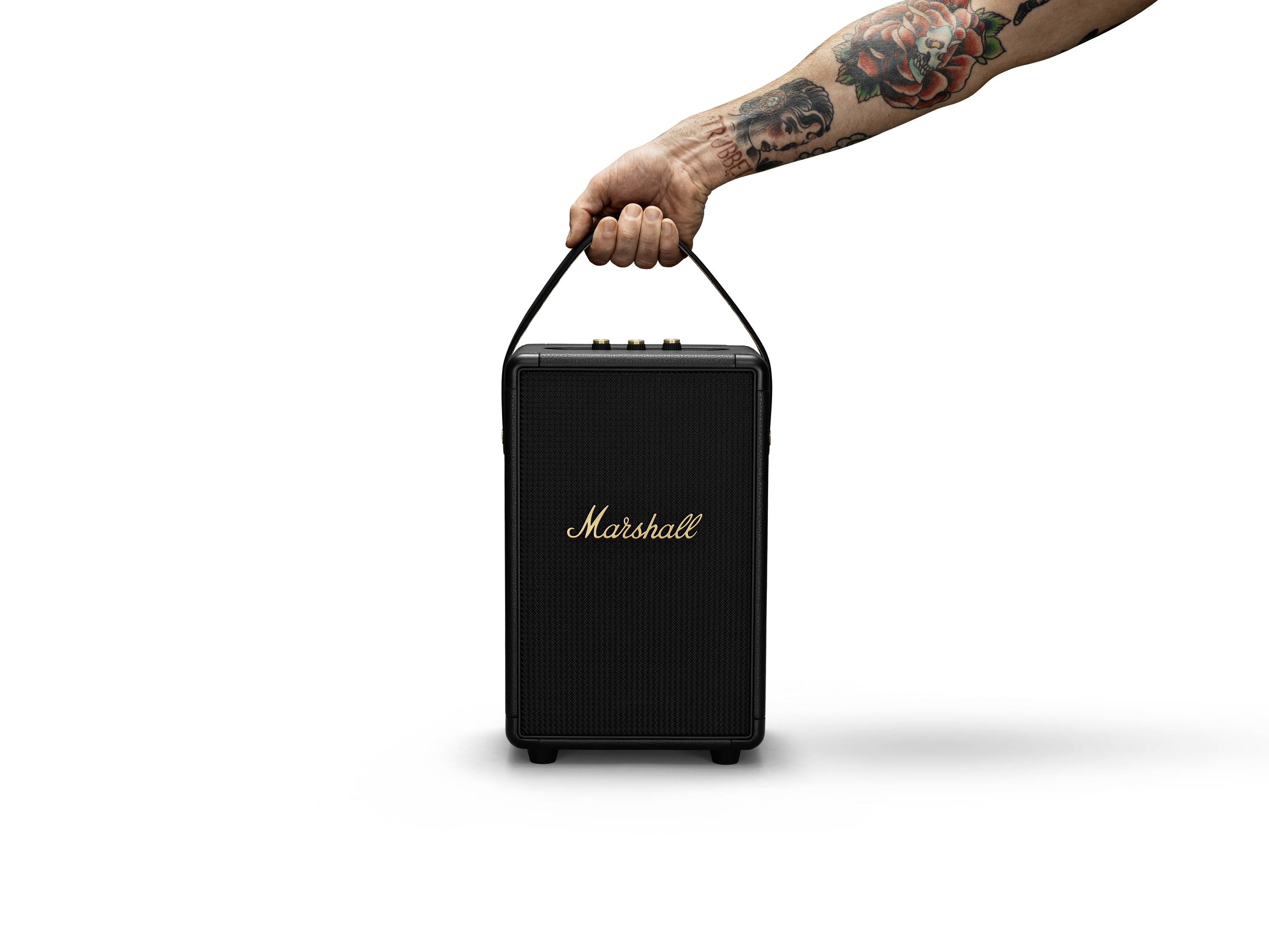 En tatoveret arm holder en sort Marshall-højttaler med et håndtag. Højttaleren har et enkelt, rektangulært design.