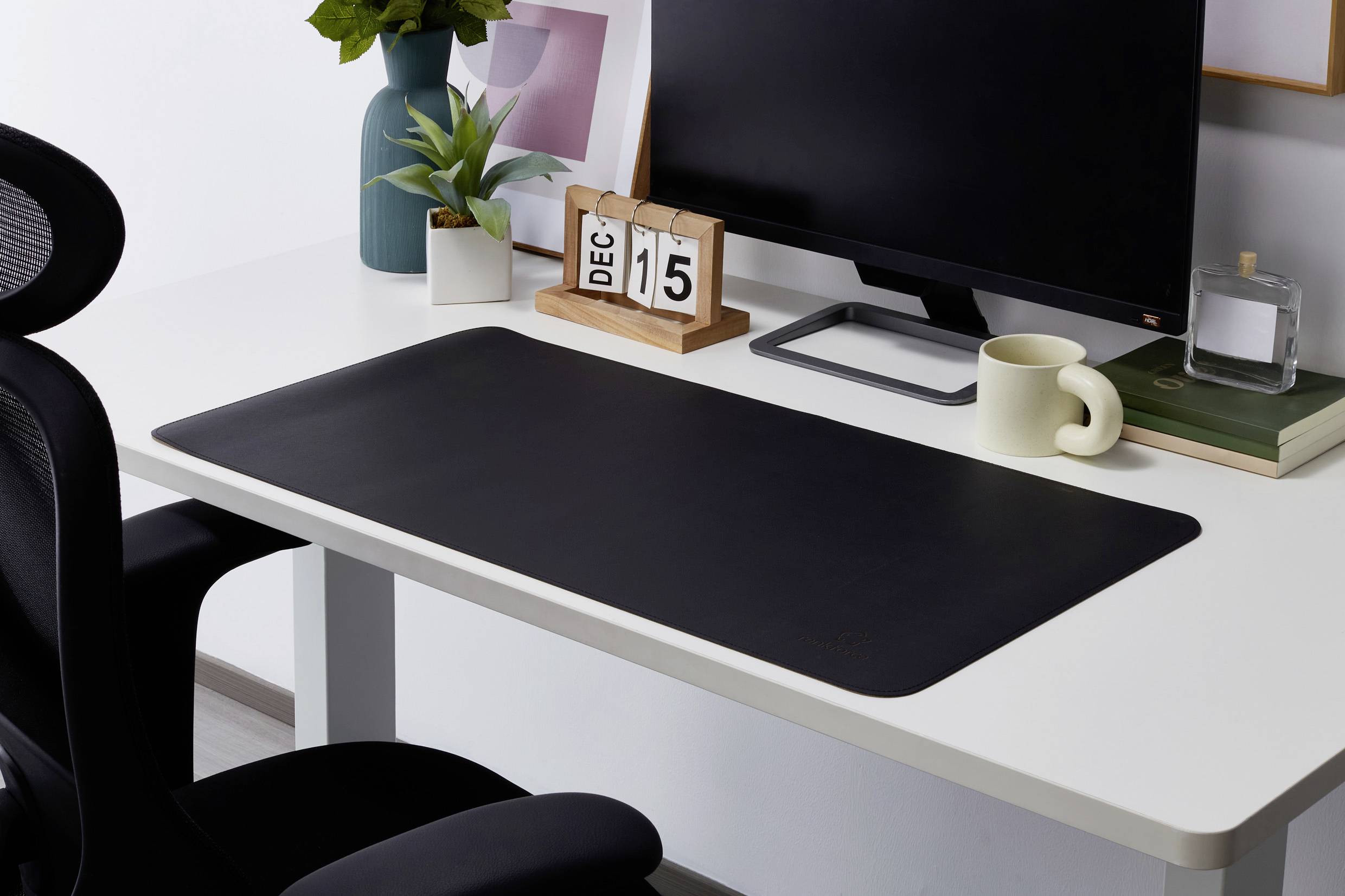 Moderne skrivebord med skærm, kontorstol, sort skriveunderlag, planter og kalender, der viser '15. dec'.