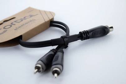 Et sort audiokabel med en adapter, præsenteret på en blå overflade. Til venstre ses en brun papæske.