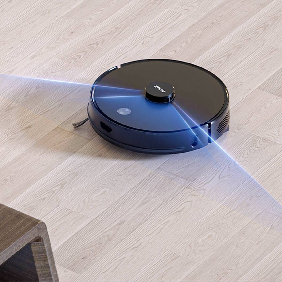 En rund støvsugerobot på trægulv navigerer med en blå laststråle. Den bevæger sig tæt på et bordben.