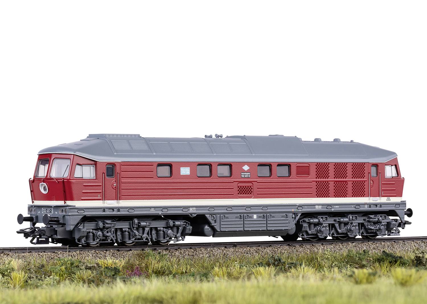 Rødt model af et diesellokomotiv på et jernbanespor med en grøn-brun englandskab i forgrunden.