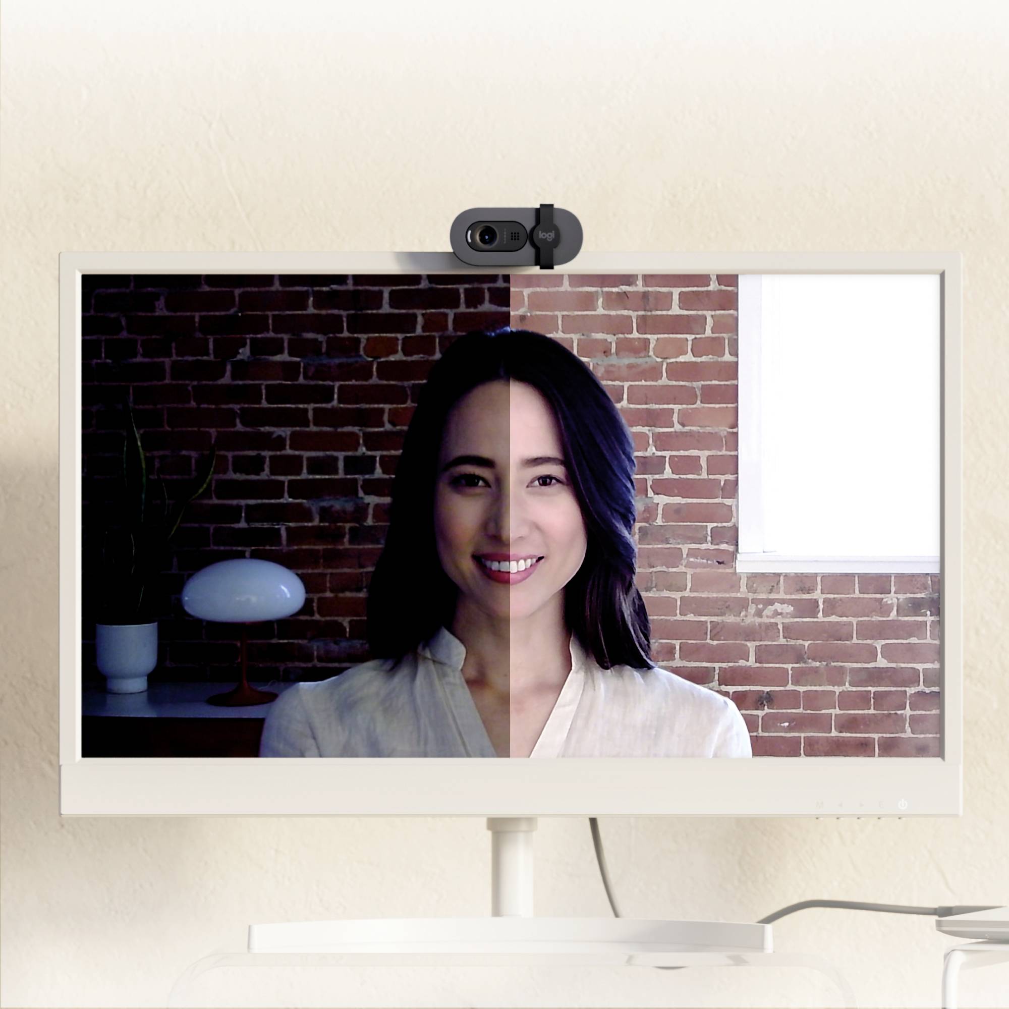 En person på en delt skærm med forskellige belysningsforhold. Venstre side mørkere, højre side lysere. Personen smiler. Webcam øverst.