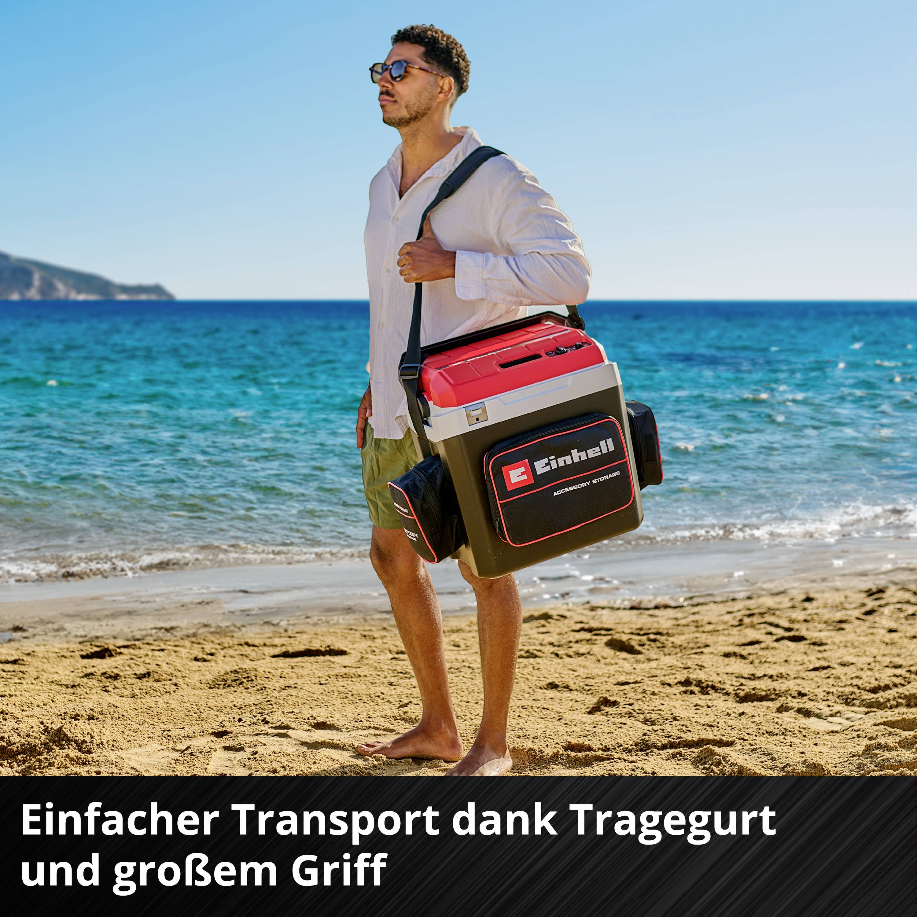 En mand på stranden bærer en kasse med bærestrop. På kassen står der 'Einhell'. Tekst: 'Nem transport takket være bærestrop og stort håndtag'.