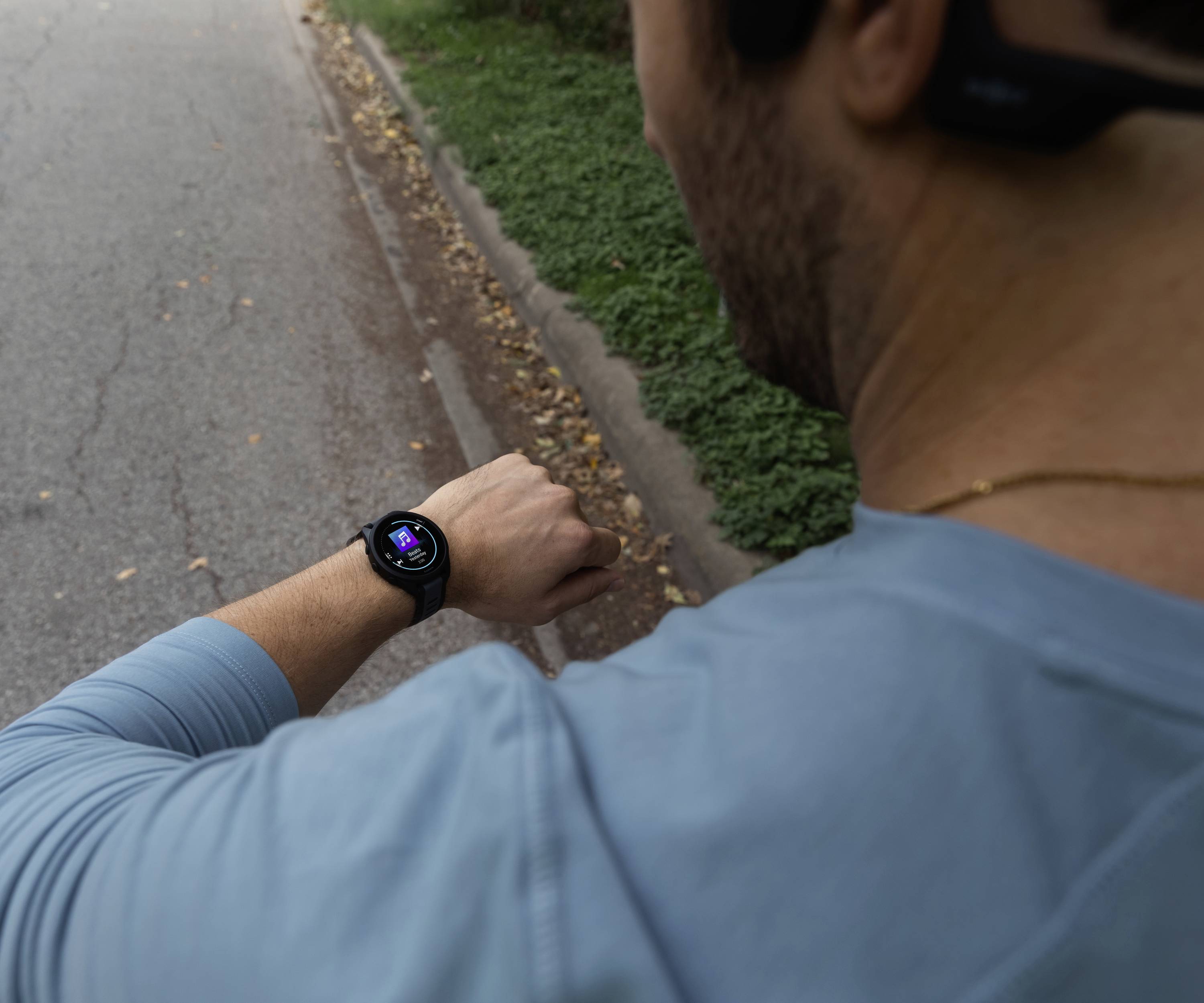 En mand i sportsøj kigger ned på sin smartwatch under løb, mens den viser træningsdata. Han befinder sig på en vej.