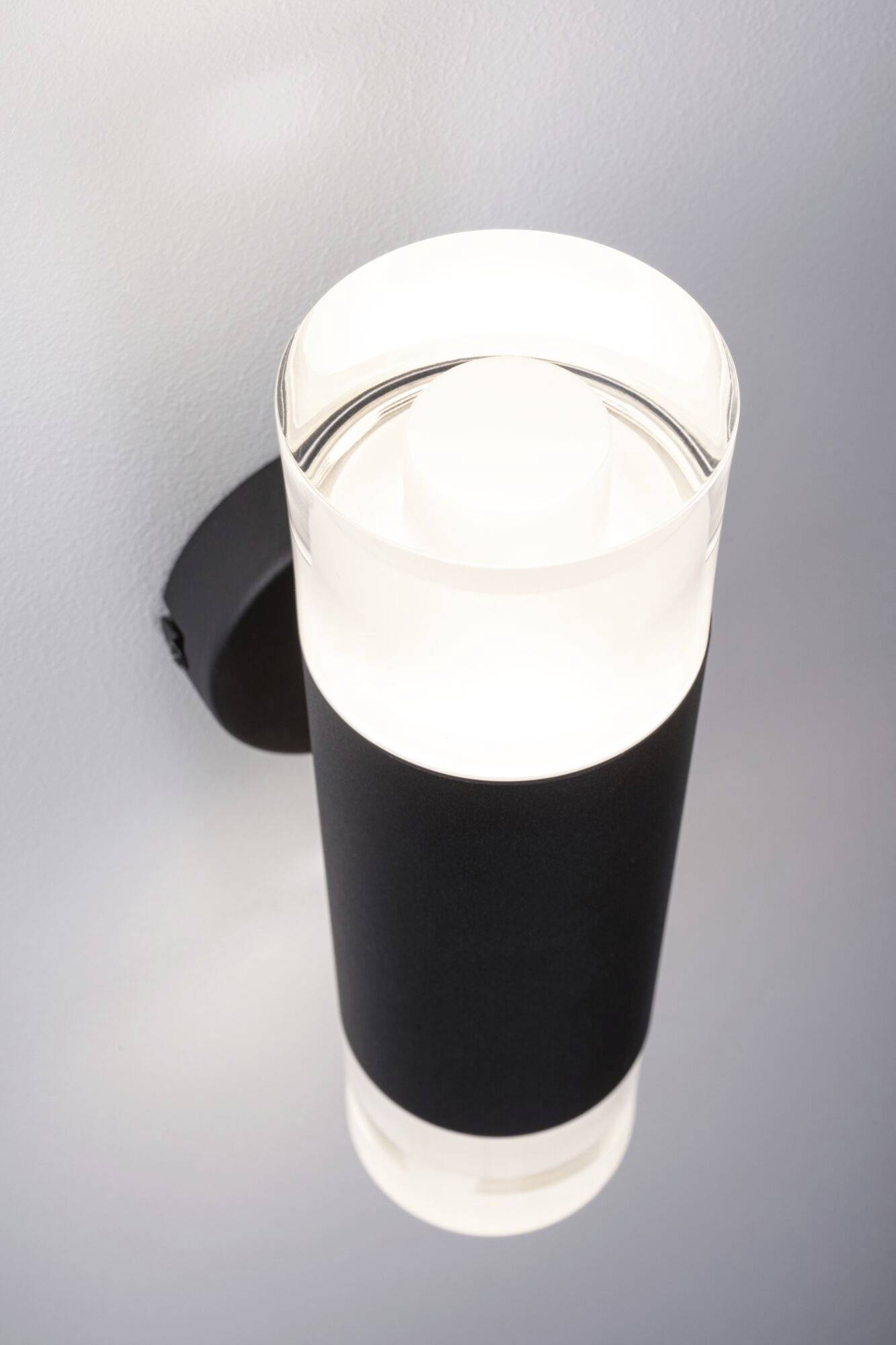 En moderne væglampe med cylinderformet design, sort kabinet og et lysende, klart lys, monteret på en væg.