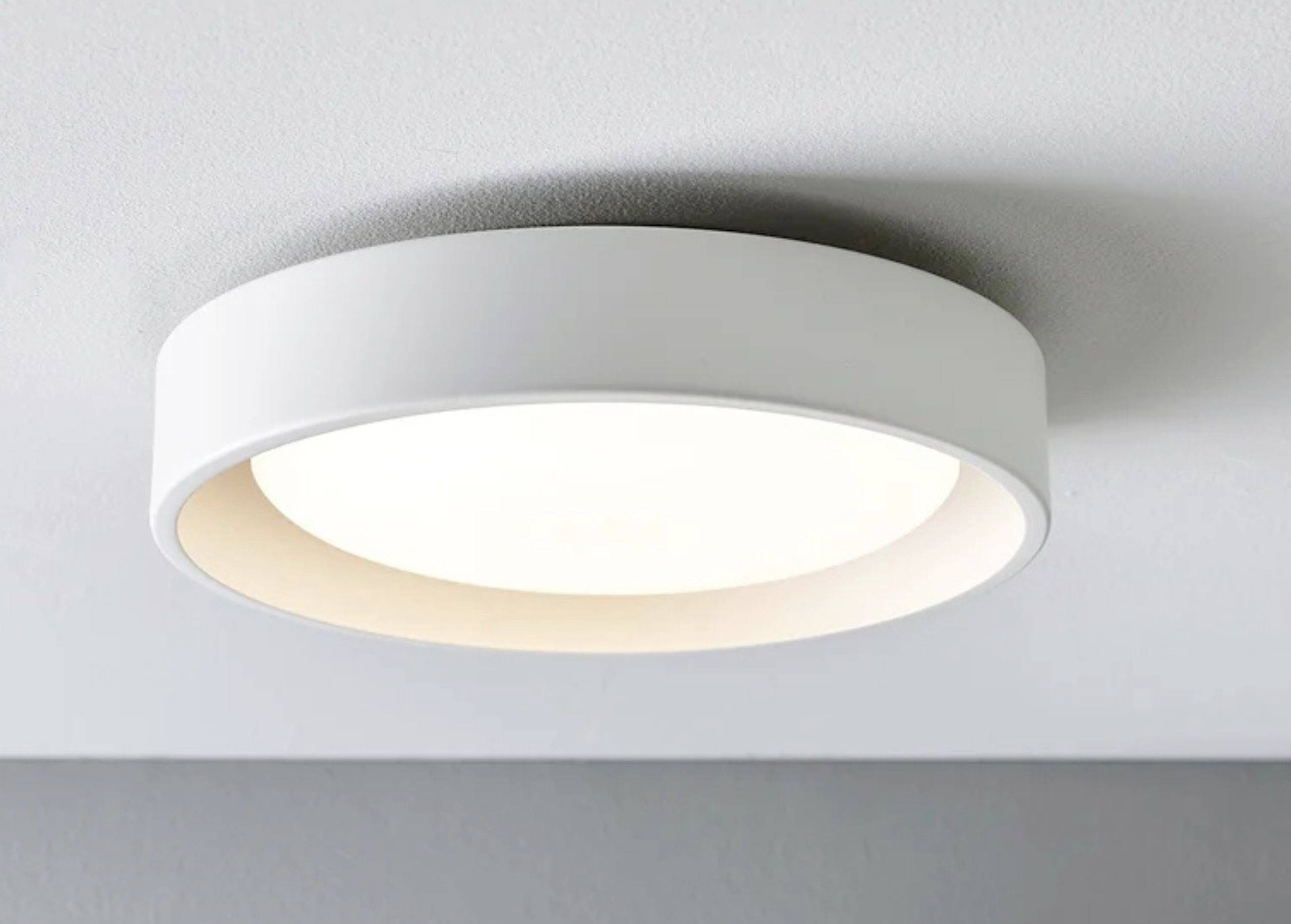 Hvid, rund loftlampe med moderne design, monteret i loftet, som lyser klart og jævnt.
