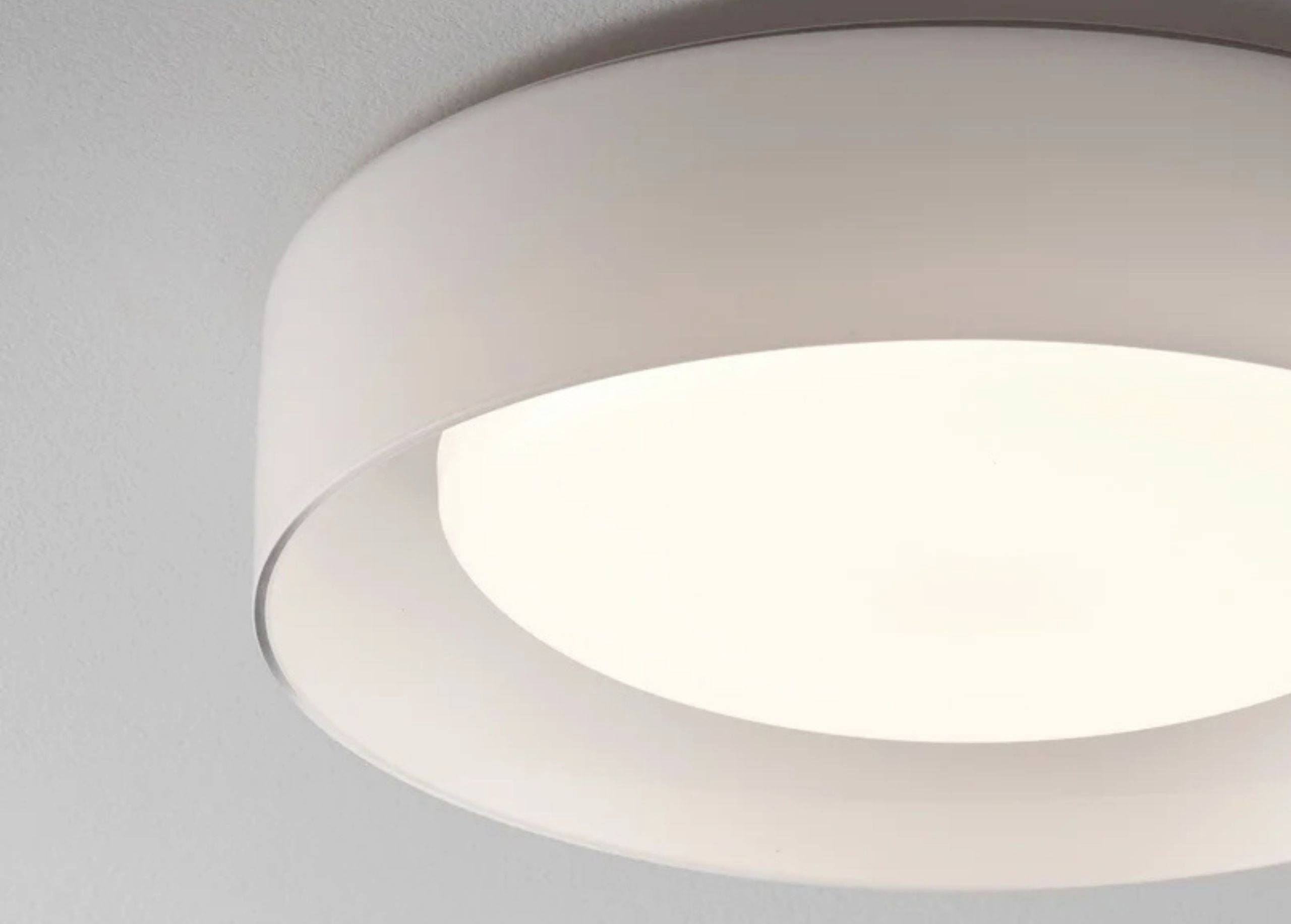 Rund, moderne loftslampe med hvid ramme og diffus lysudbredelse i et rum.