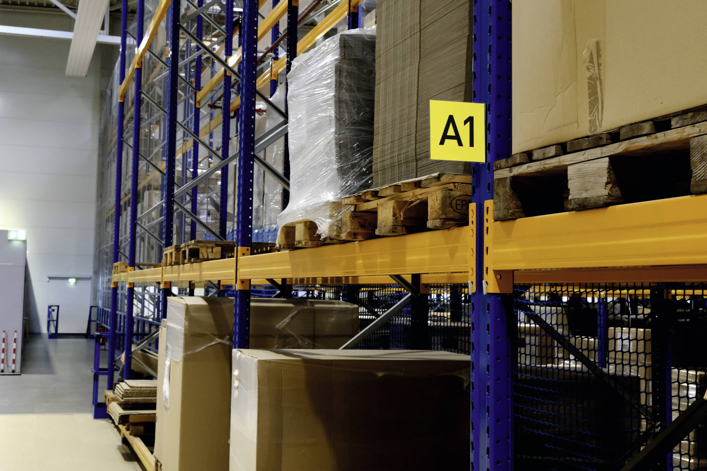 Reolsystem med paller, begyndende fra 'A1'. Høje hylder med emballerede varer i et lagerrum.