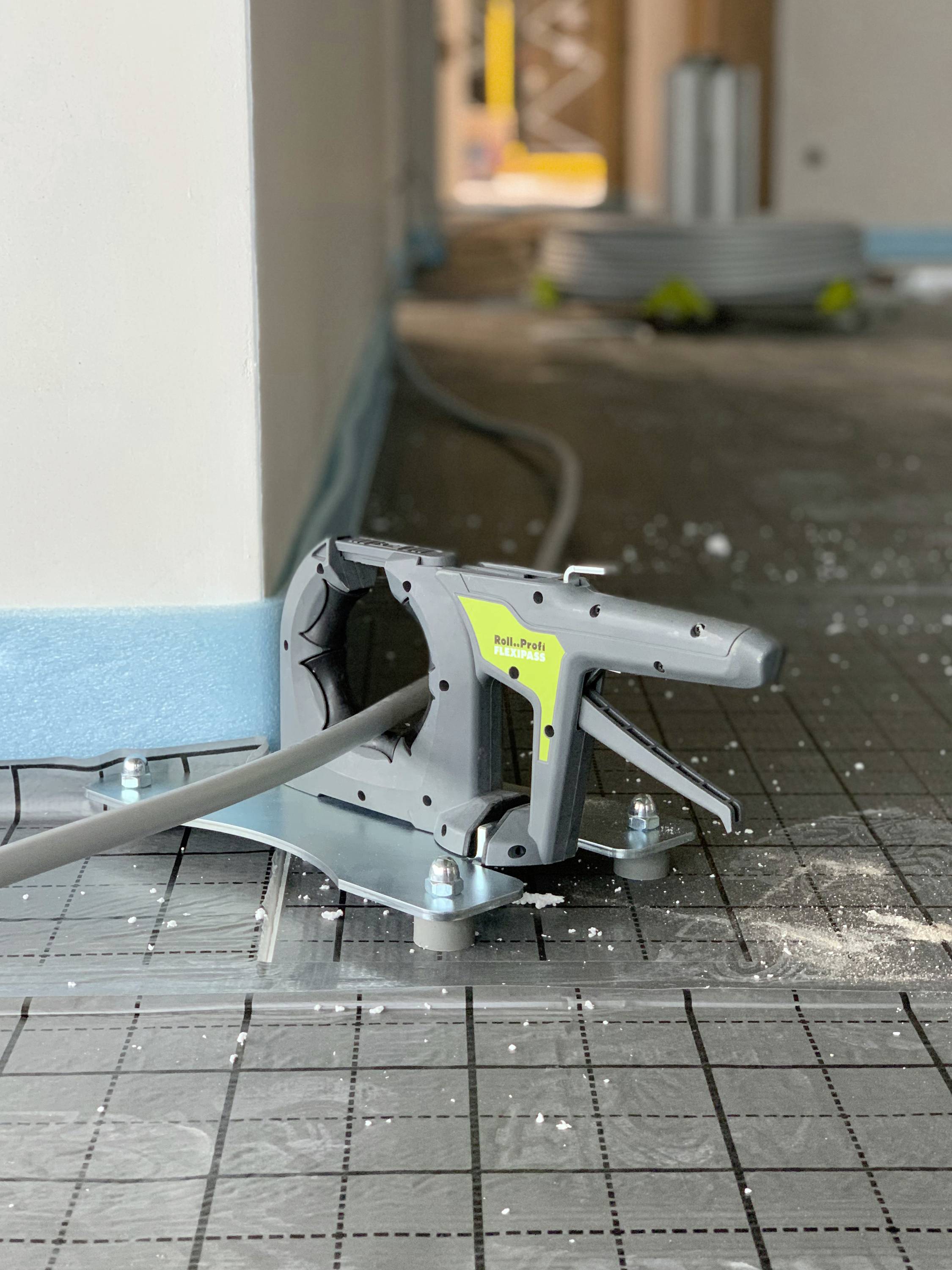 En kabeltrækningmaskine ligger på et flisegulv og trækker kabler gennem et gråt rør i en bygning.
