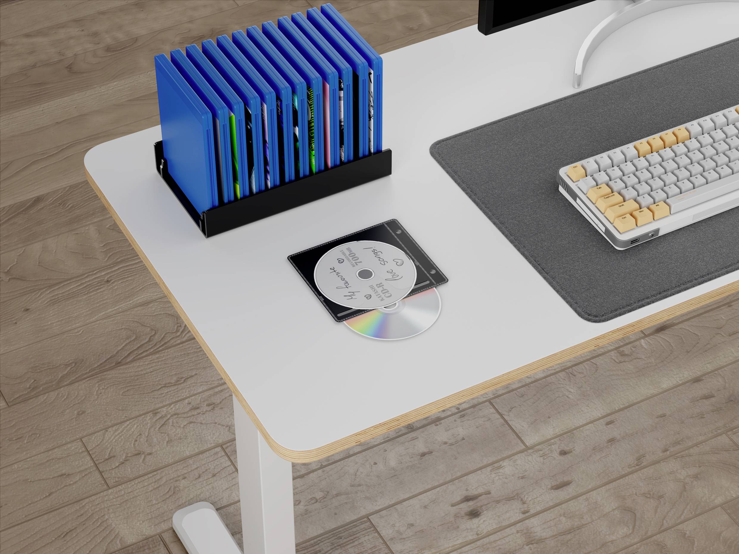 Et hvidt skrivebord med et tastatur, et mørkegråt underlag, en cd med cover og en reol med blå mapper, alt sammen placeret oven på et trægulv.