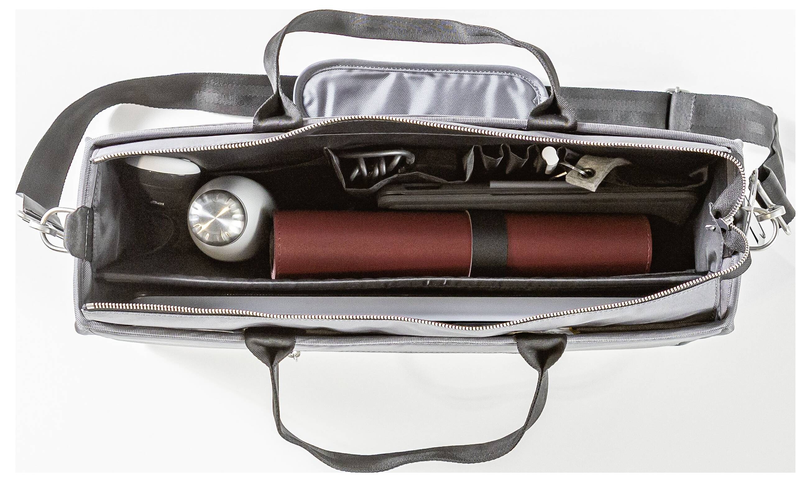 Et fugleperspektiv af en åben dokumentmappe, der viser en fyldt indvendigt rum med et cylindrisk rødt etui, en sølvfarvet termoflaske og forskellige rum.