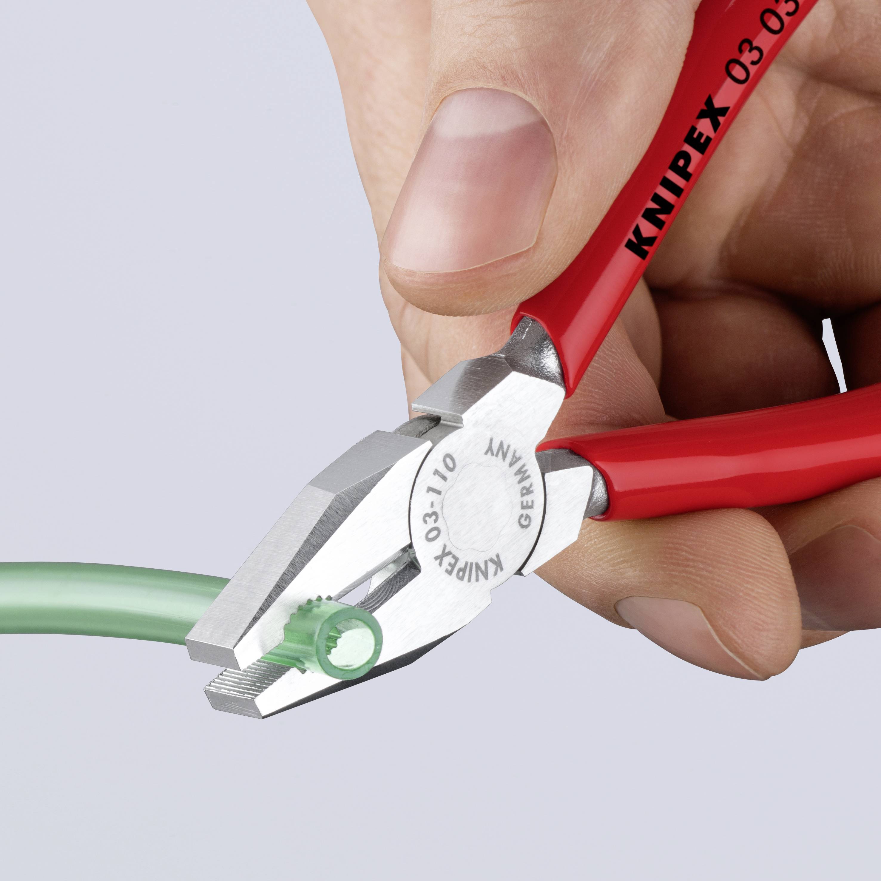 En rød tang klipper en grøn ledning. På tangen står der 'KNIPEX'. En hånd holder tangen.
