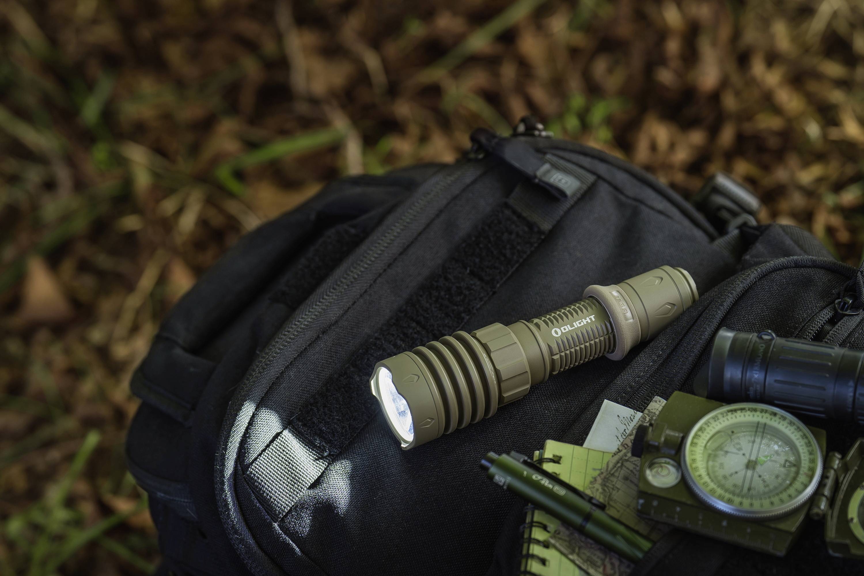 Lommelygte på en sort rygsæk i skoven, ved siden af et kompas og en notesbog. Perfekt til udendørs aktiviteter.