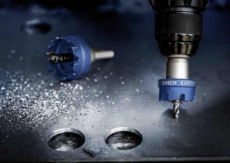 Metalbor fra Bosch med borevedhæng, borer identiske huller i metalpladen. Spåner spredt på overfladen.