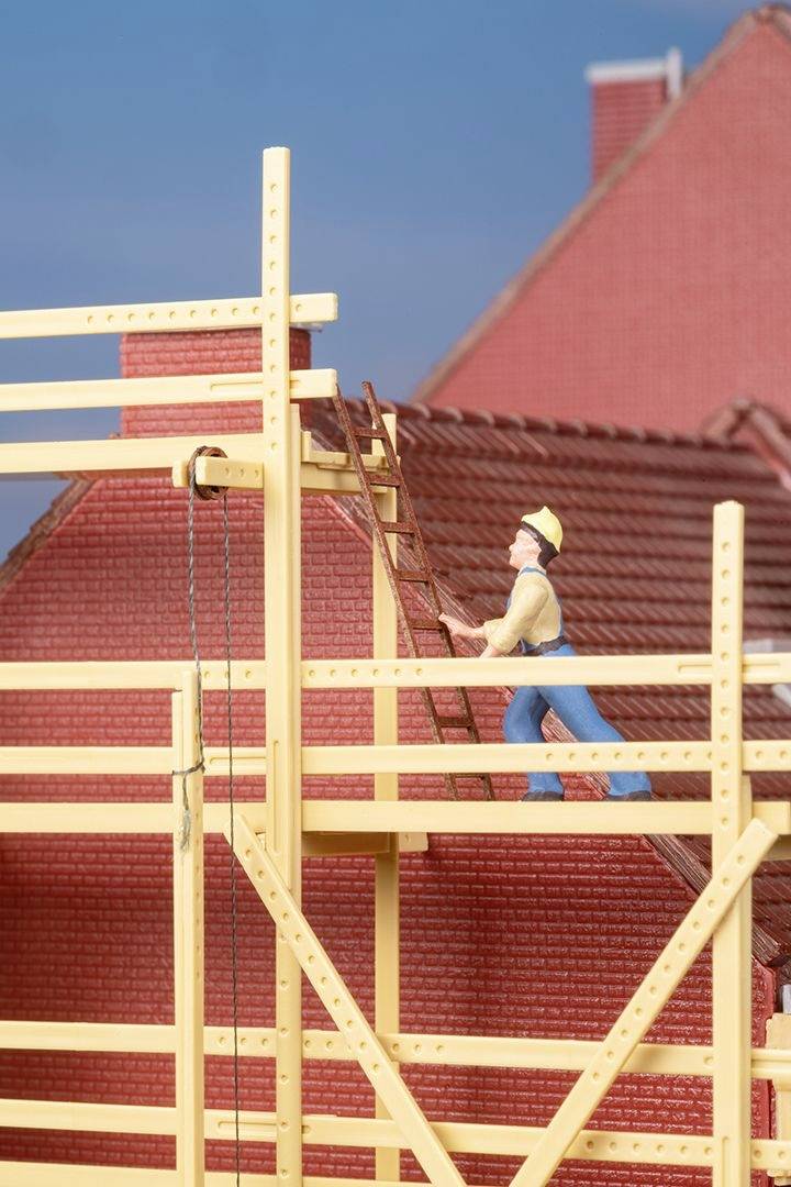 En bygningsarbejder med hjelm står på et stillads foran et hus med røde mursten og bærer en stige højere op.