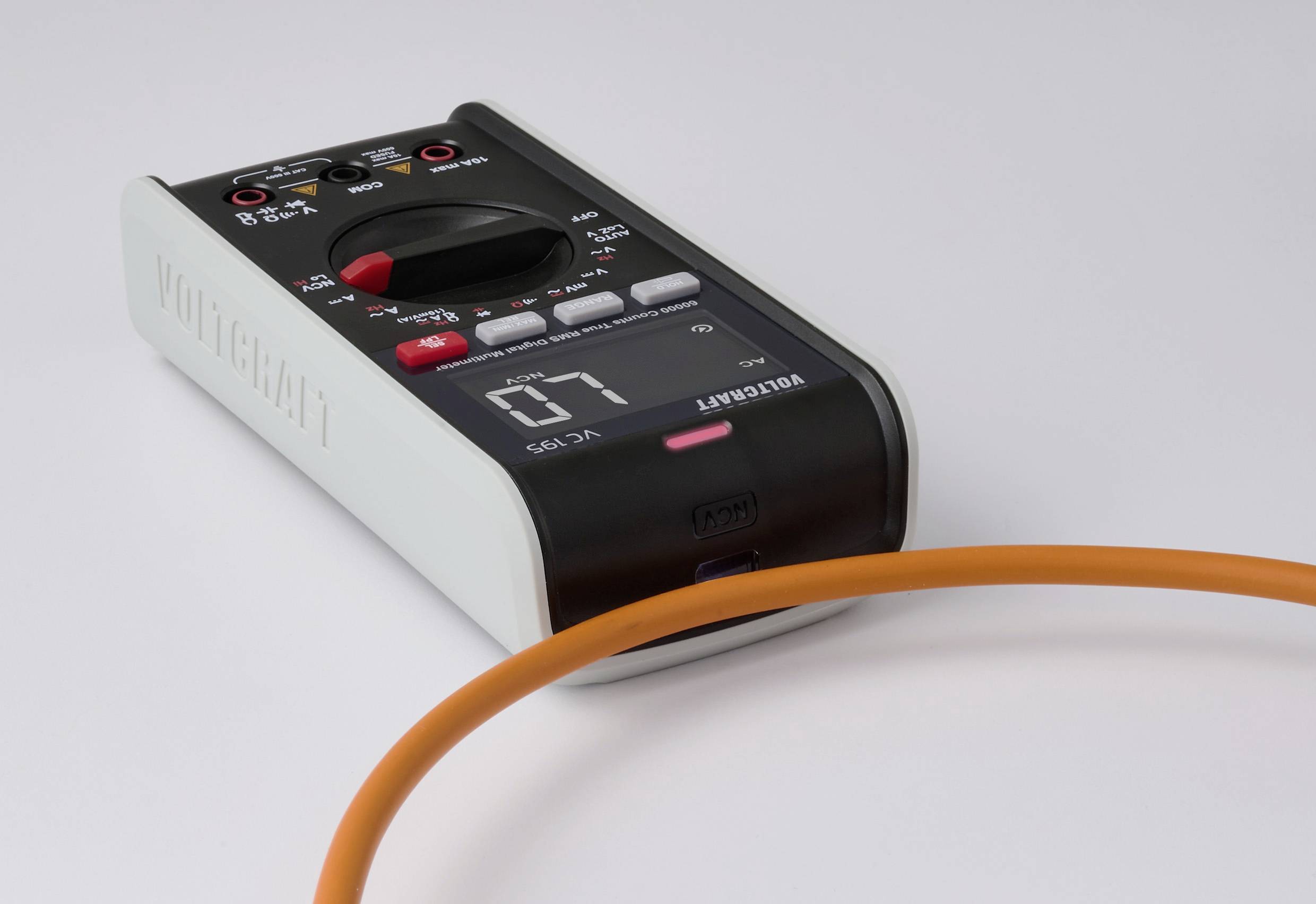 Et digitalt multimeter med et sort frontpanel, der viser '07', ligger på en overflade. En orange kabelløkke er delvist synlig i forgrunden.