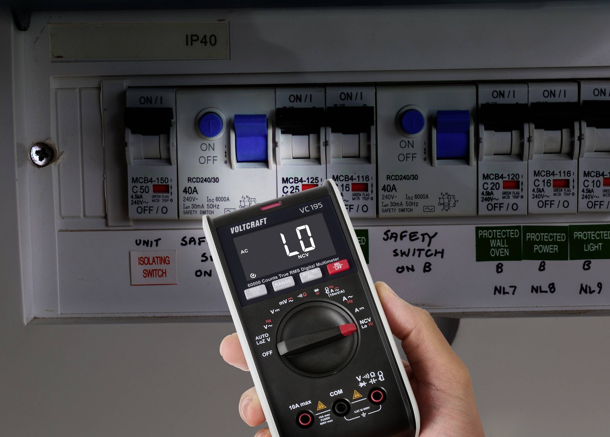 En hånd holder et digitalt multimeter, der viser 'L0' tæt på en eldistributionstavle med flere automatsikringer mærket 'MCB4-125' og 'RCBO40MLH'.