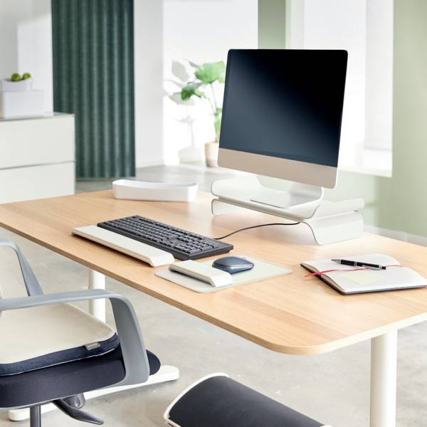 Moderne arbejdsplads med computer, tastatur og notesbog på et træskrivebord. I baggrunden ses planter.