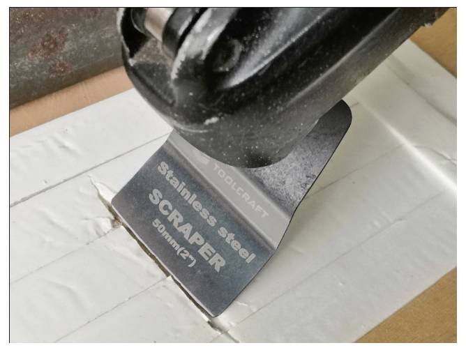 En rustfri skraberstang mærket 'Rustfri stål SKRABER 90mm (3")' skærer gennem en overflade.