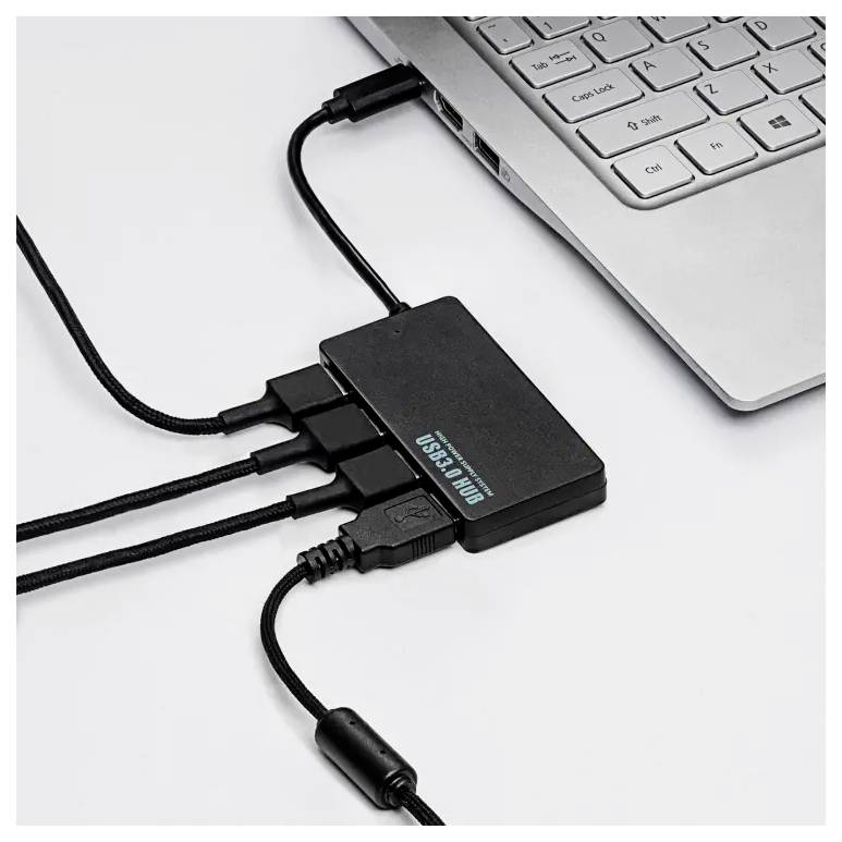 USB-hub med fire tilslutninger, forbundet til en laptop. Tre kabler er tilsluttet. Hubben er sort og rektangulær.
