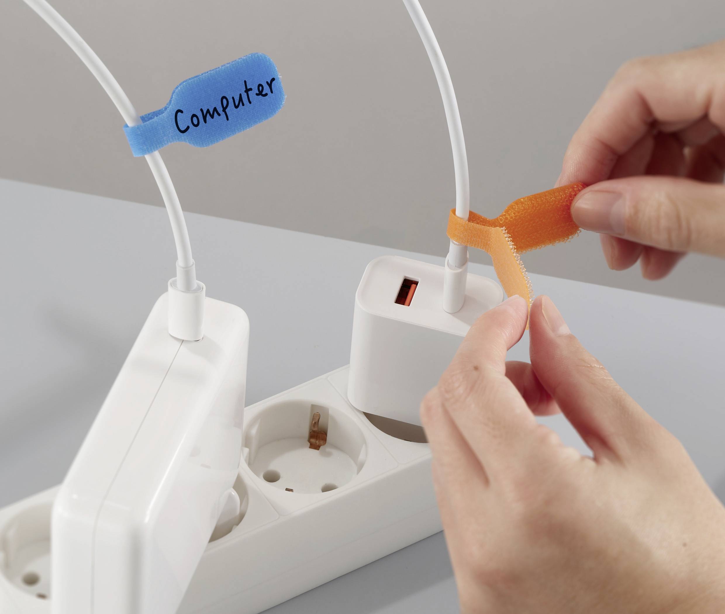 En person påsætter et orange mærkat på en ledning, mens en anden ledning med et blåt mærkat, hvorpå der står 'Computer', er sat i et strømpanel.