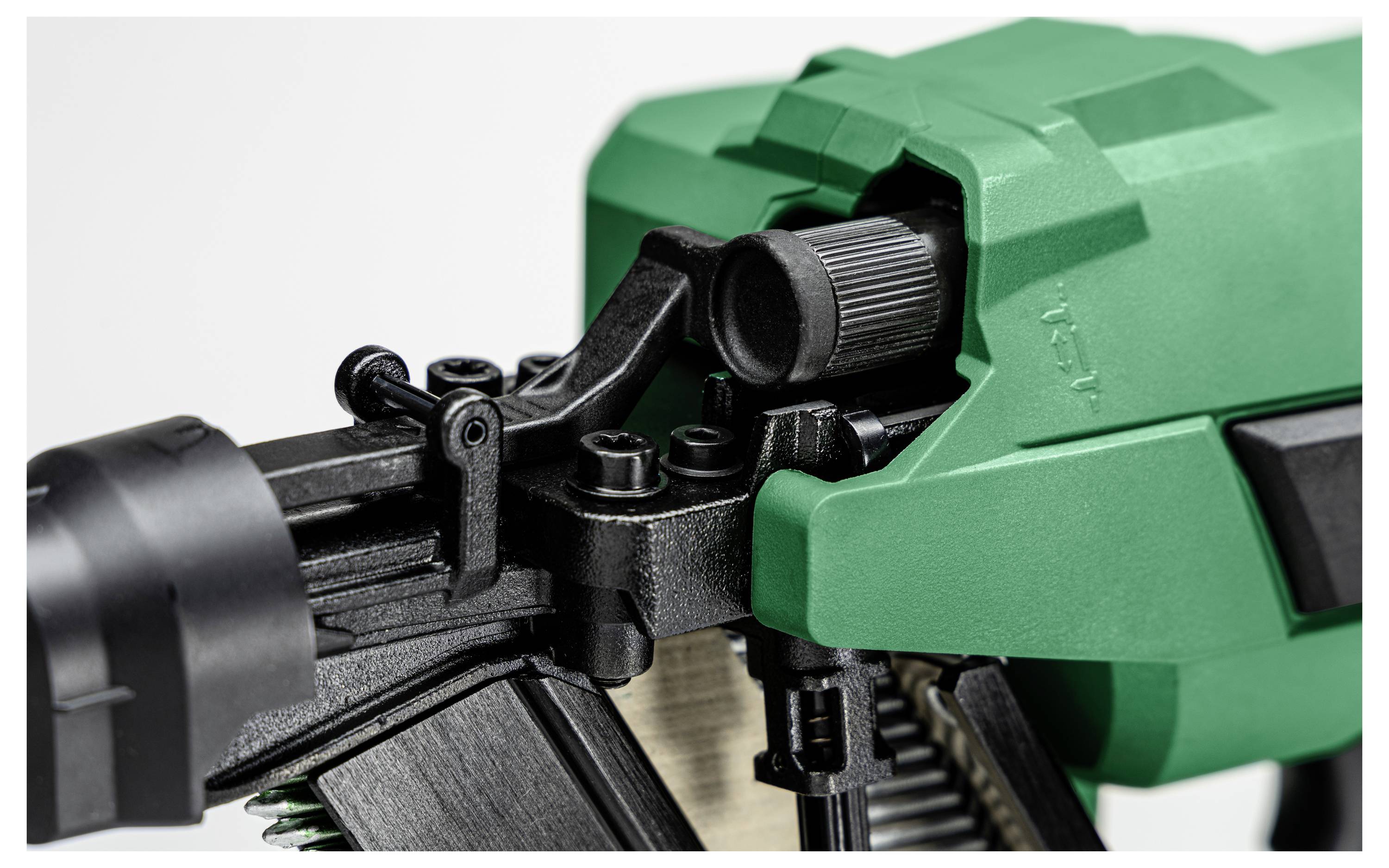 Nærbillede af en grøn og sort sømpistol, der viser justeringsdrejeskiven og udløsningsmekanismen, hvilket fremhæver dens konstruktion og funktionalitet.